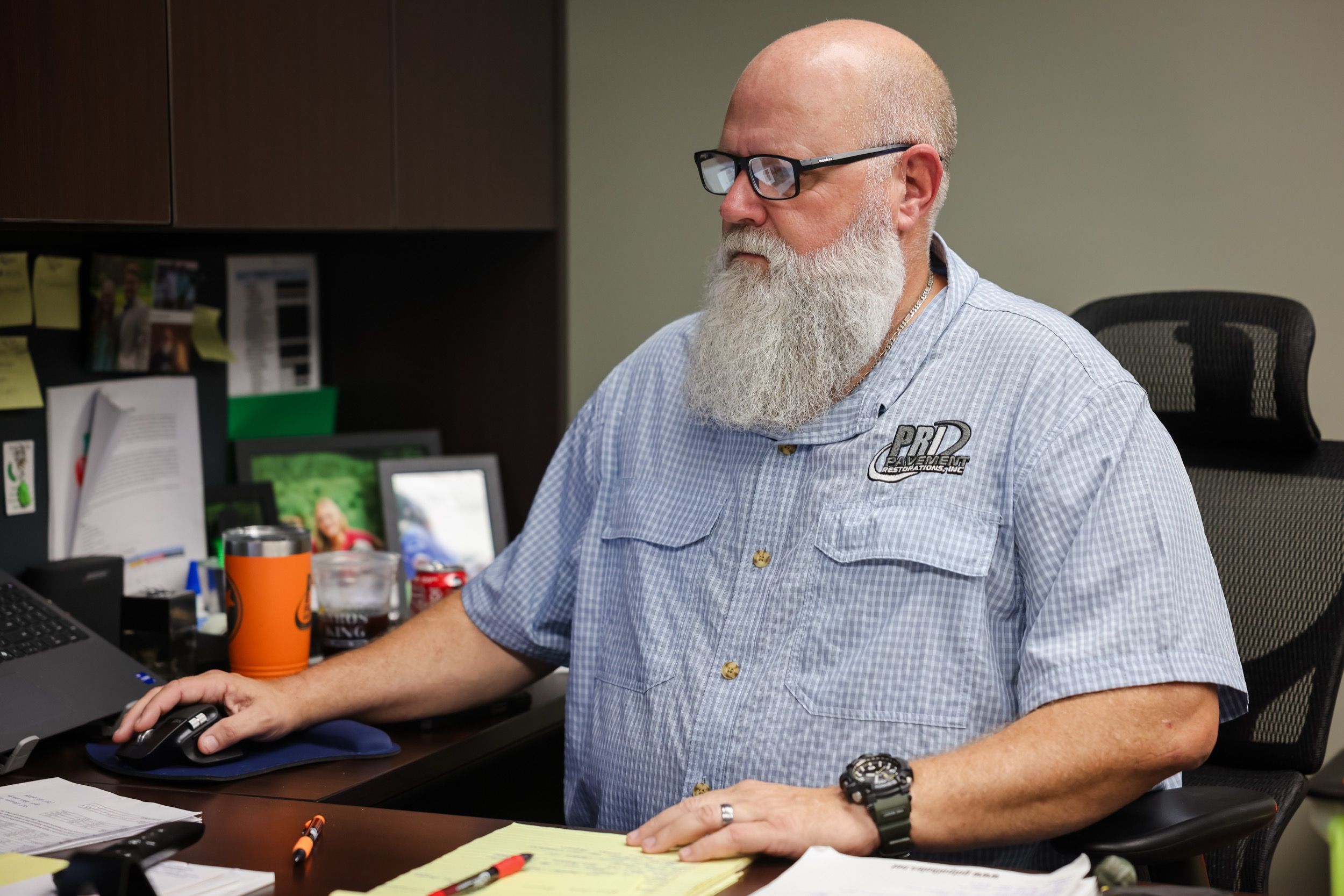 Man with a white beard and glasses working at a desk using a computer mouse.