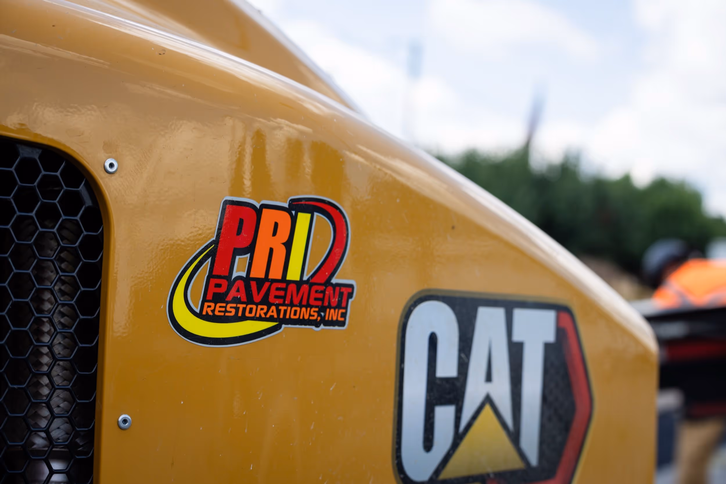 Close-up of yellow construction equipment with a PRD Pavement Restorations, Inc. sticker and a CAT logo.
