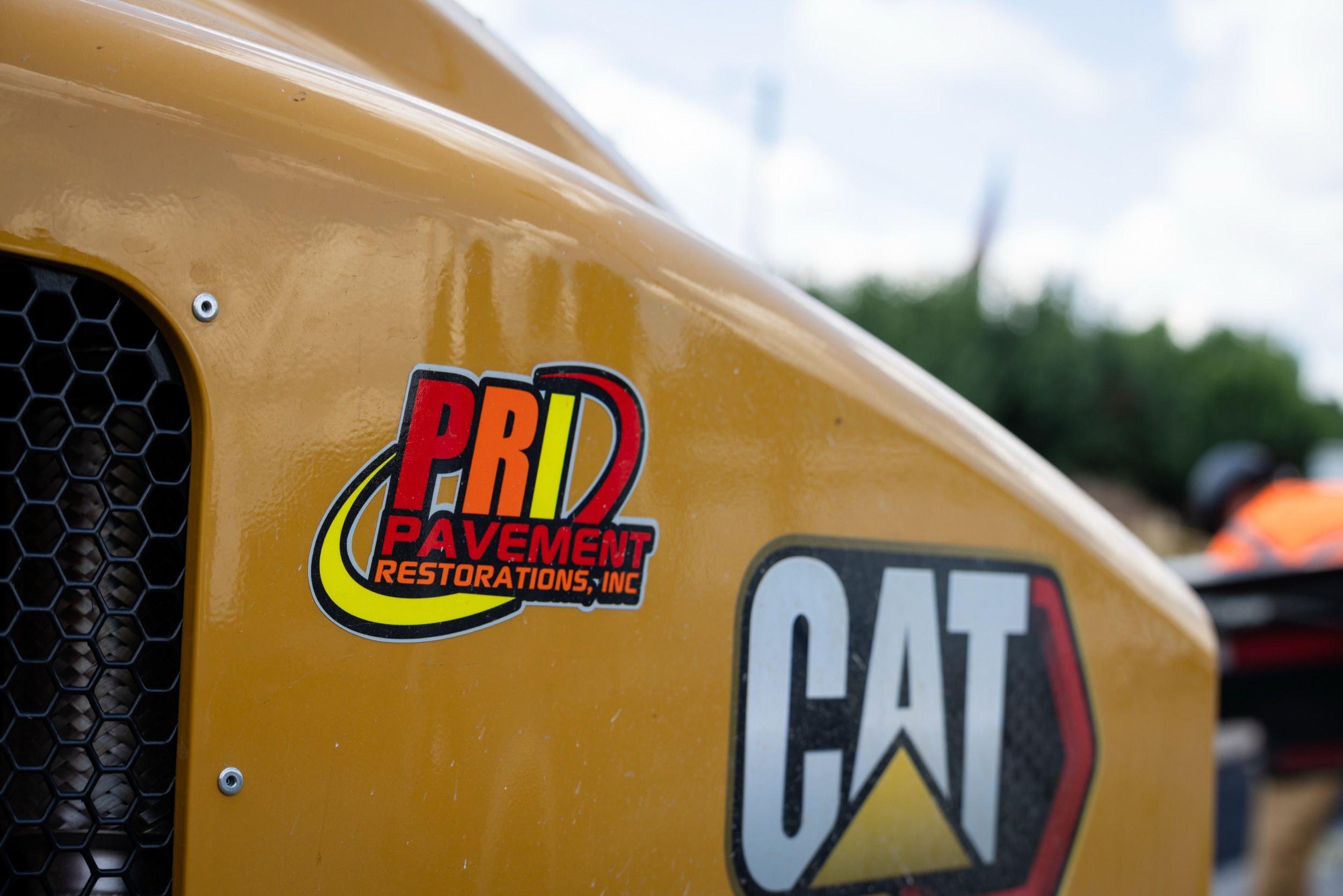 Close-up of yellow construction equipment with a PRD Pavement Restorations, Inc. sticker and a CAT logo.