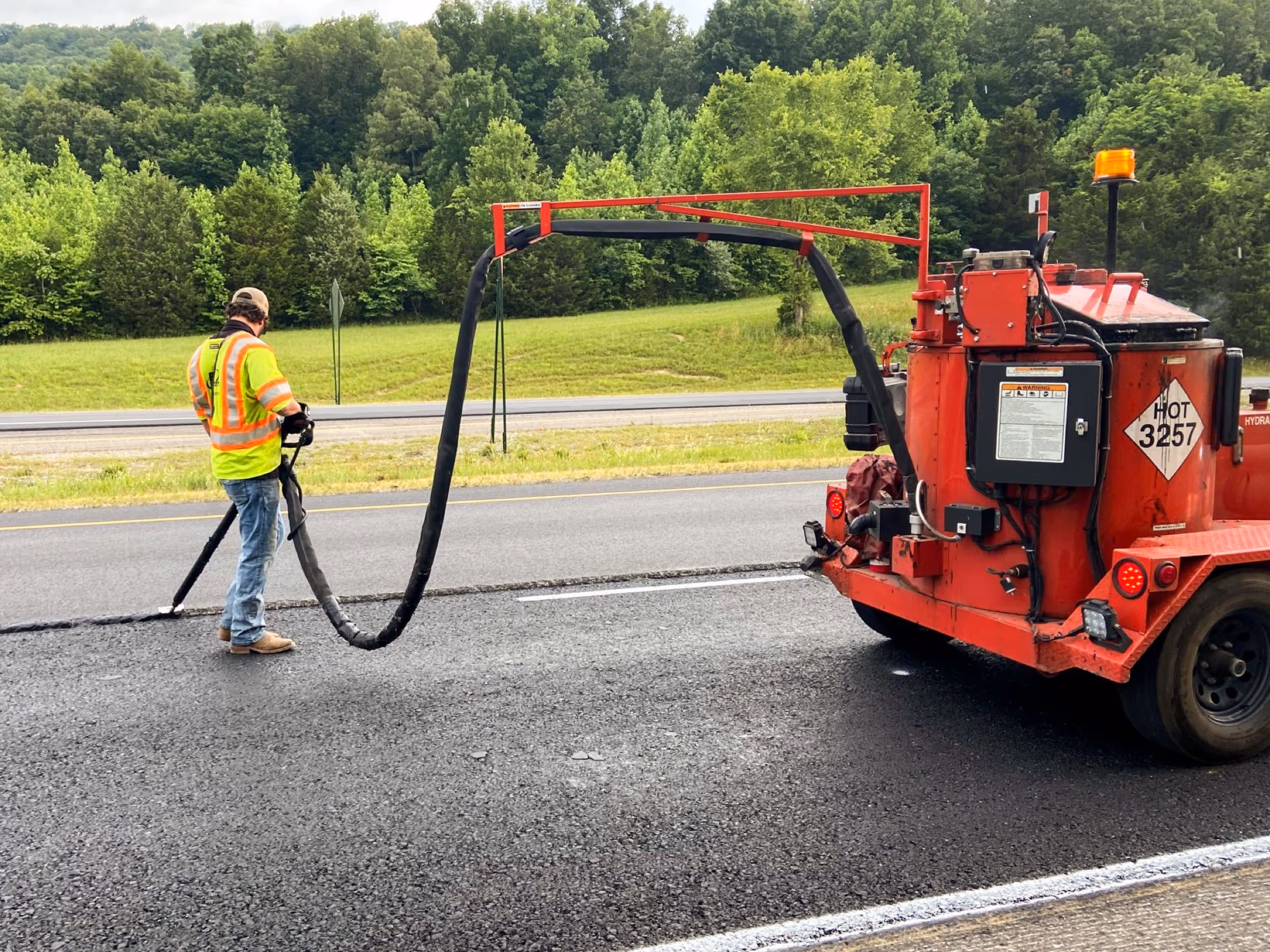 Aerial view of road paving machinery and workers laying fresh asphalt next to a green and blue tennis court.