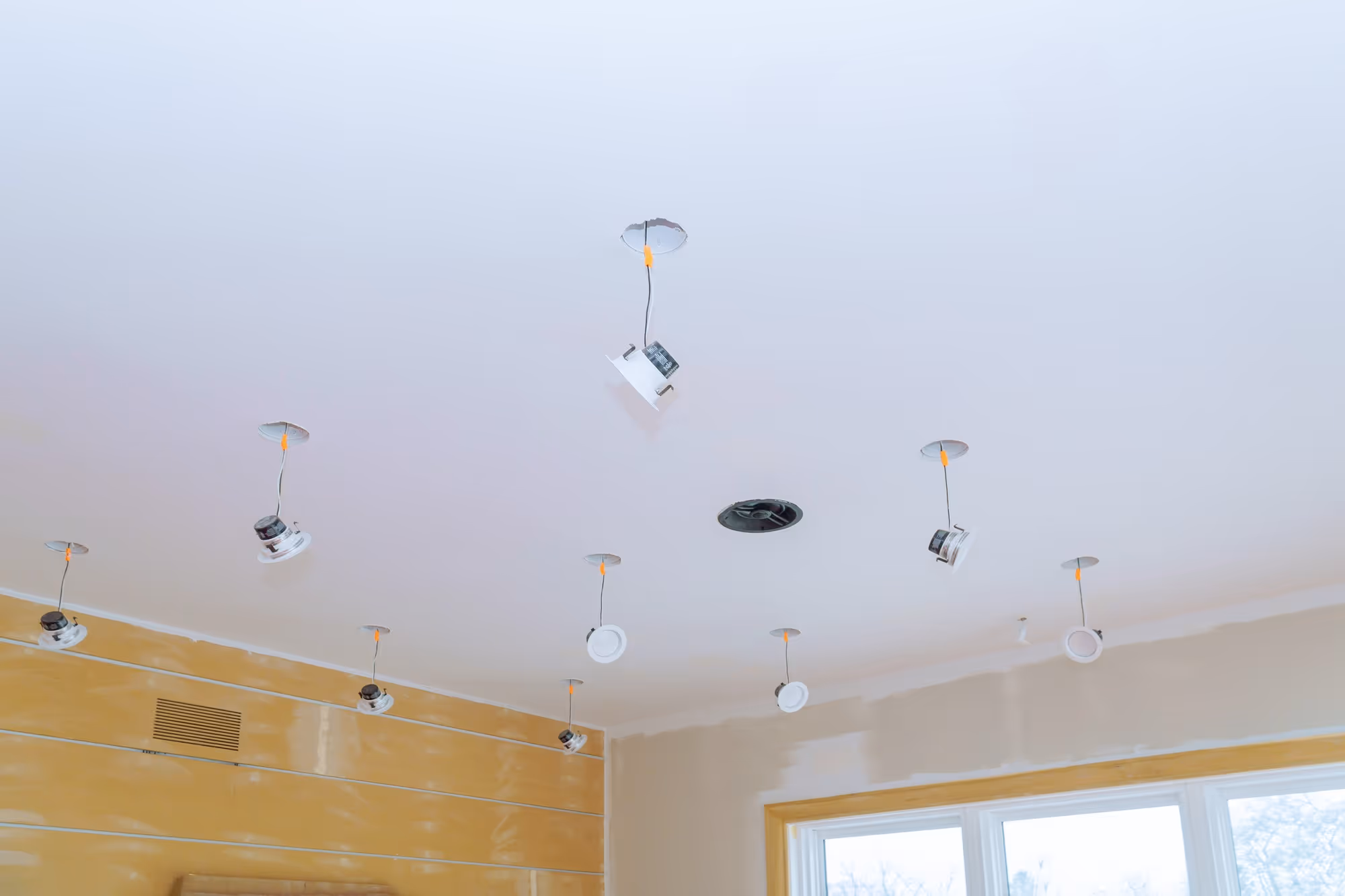 Several recessed lights installed in a ceiling with exposed wires during a renovation in a room.