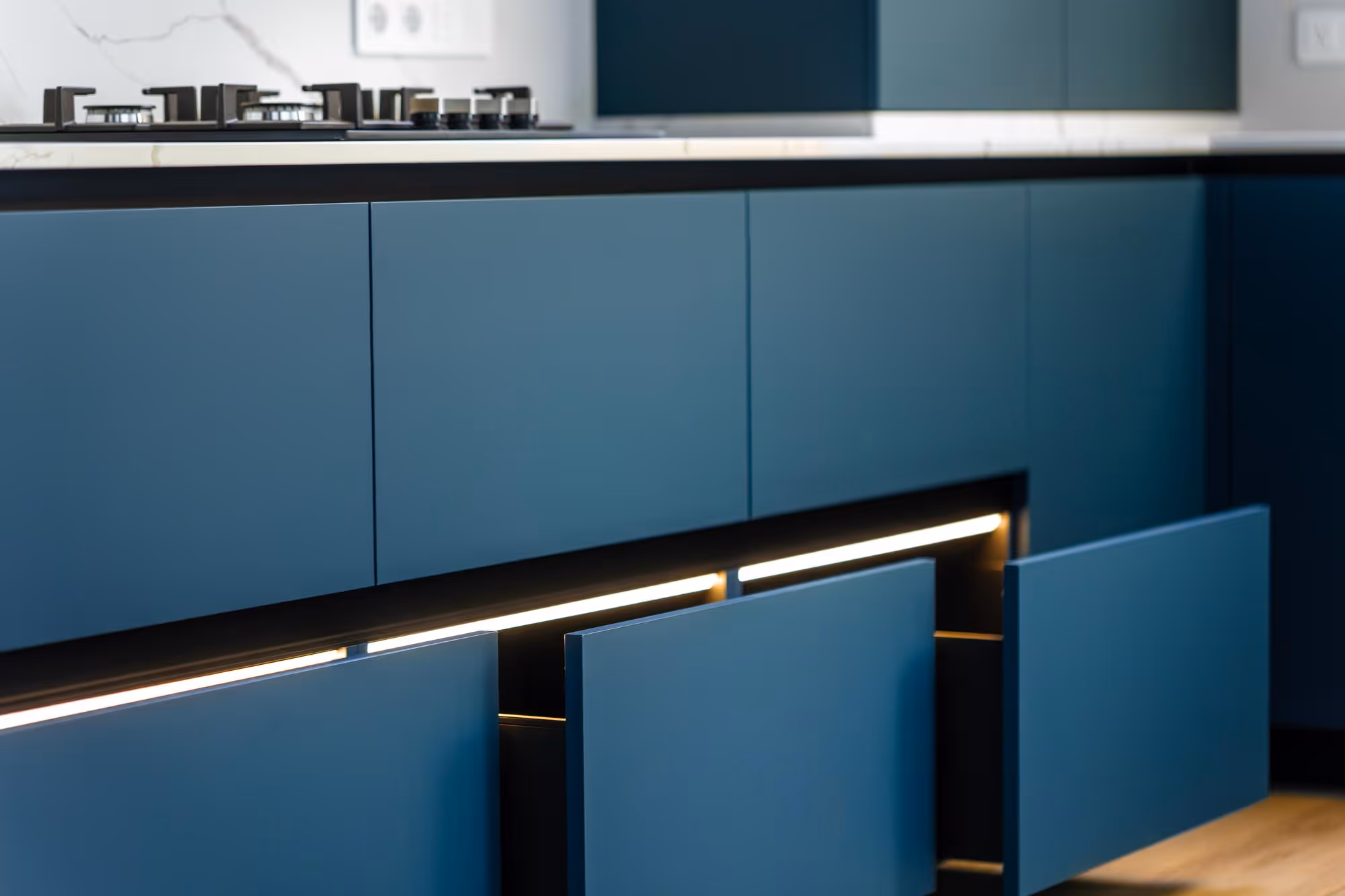 Open blue kitchen drawers with under-cabinet lighting, featuring a modern stove on the countertop.