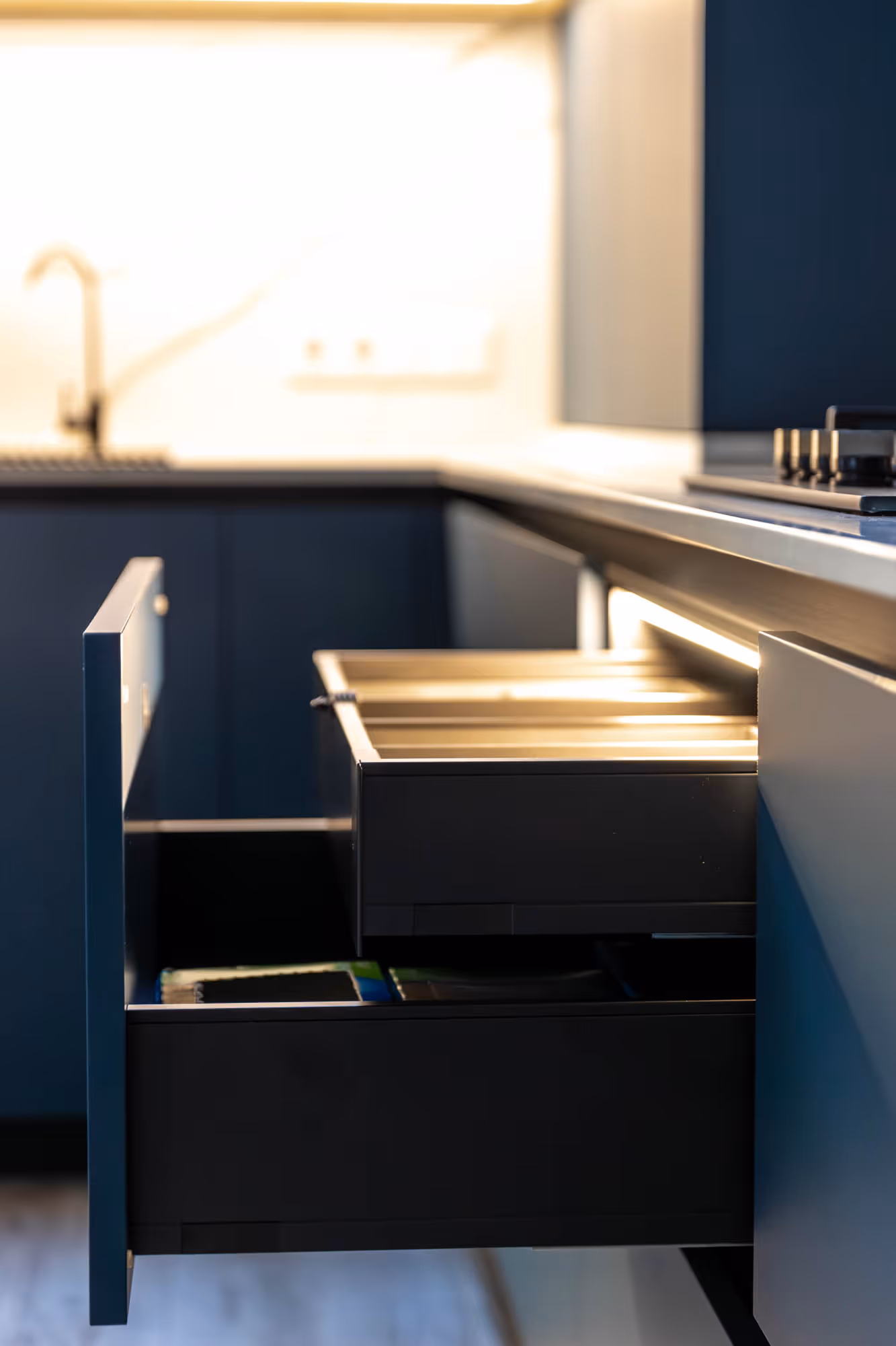Two open kitchen drawers with silverware and utensils inside, beneath a counter in a modern kitchen.