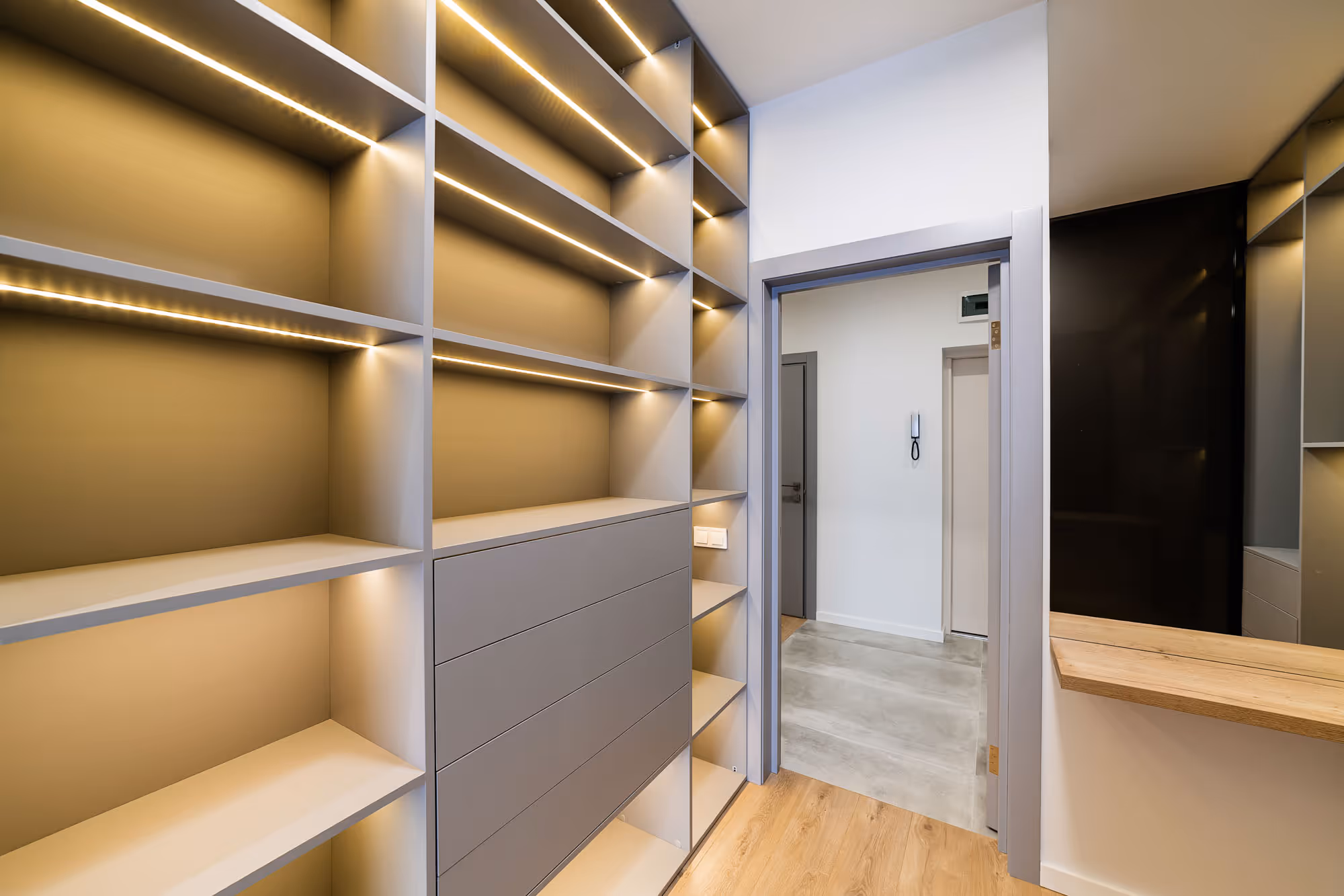 Empty modern closet with built-in shelves and drawers, featuring overhead and side lighting.