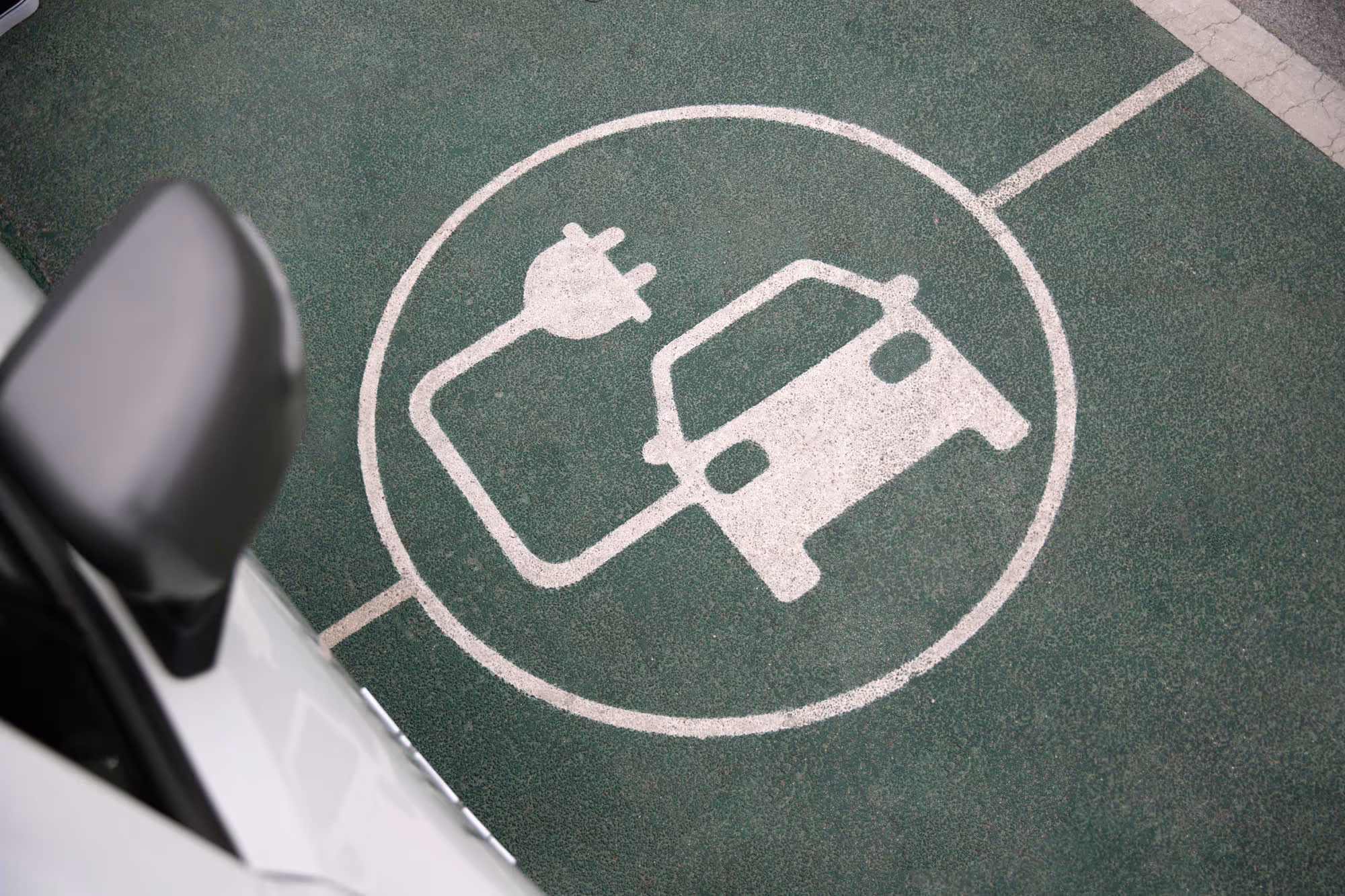 An electric vehicle parking spot marked with a white charging symbol on green pavement.