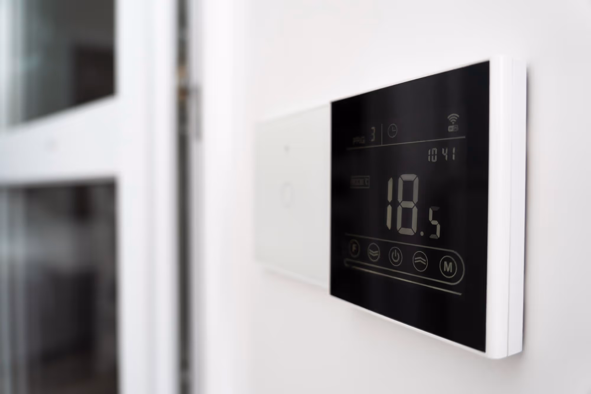 Digital thermostat displaying 18.5 degrees Celsius on a white wall.