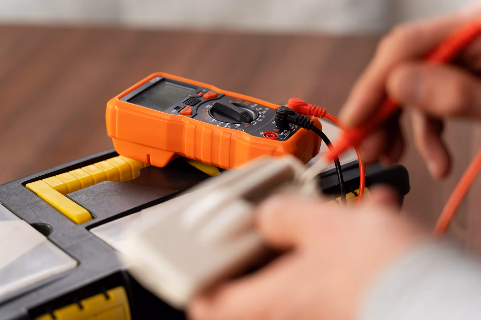 A person uses a digital multimeter to test an electrical device on a workbench.