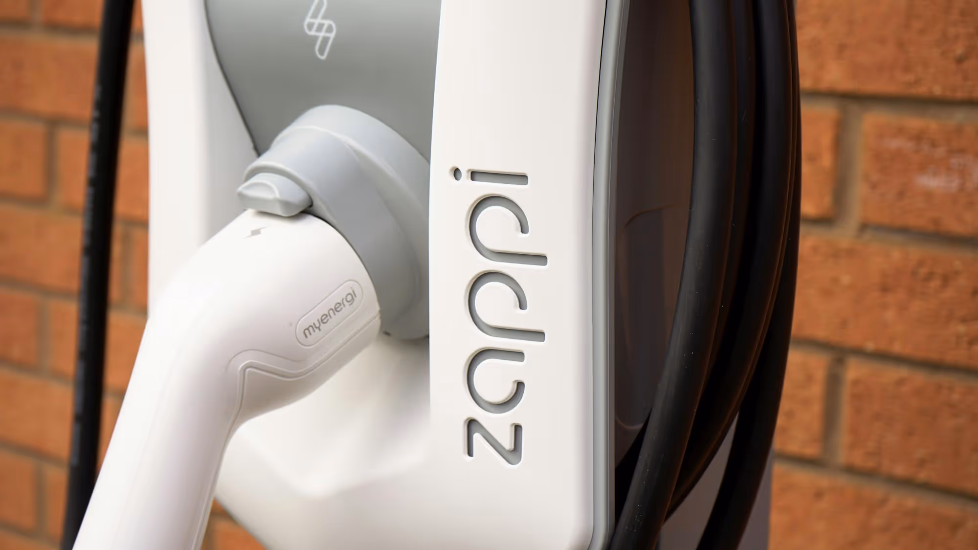 An electric vehicle charging plug is connected to a wall-mounted charging station with "zappi" branding.