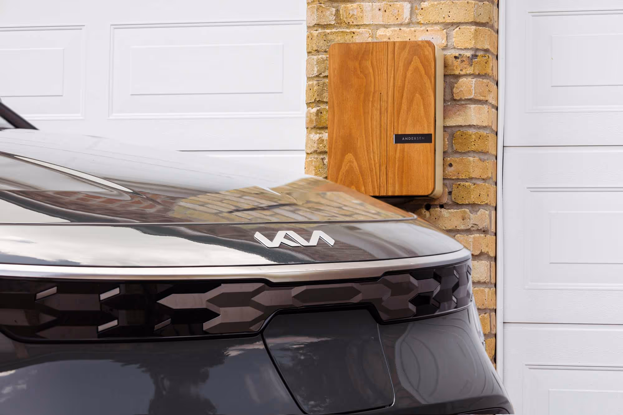 Electric car parked near a wooden charging station mounted on a brick wall.