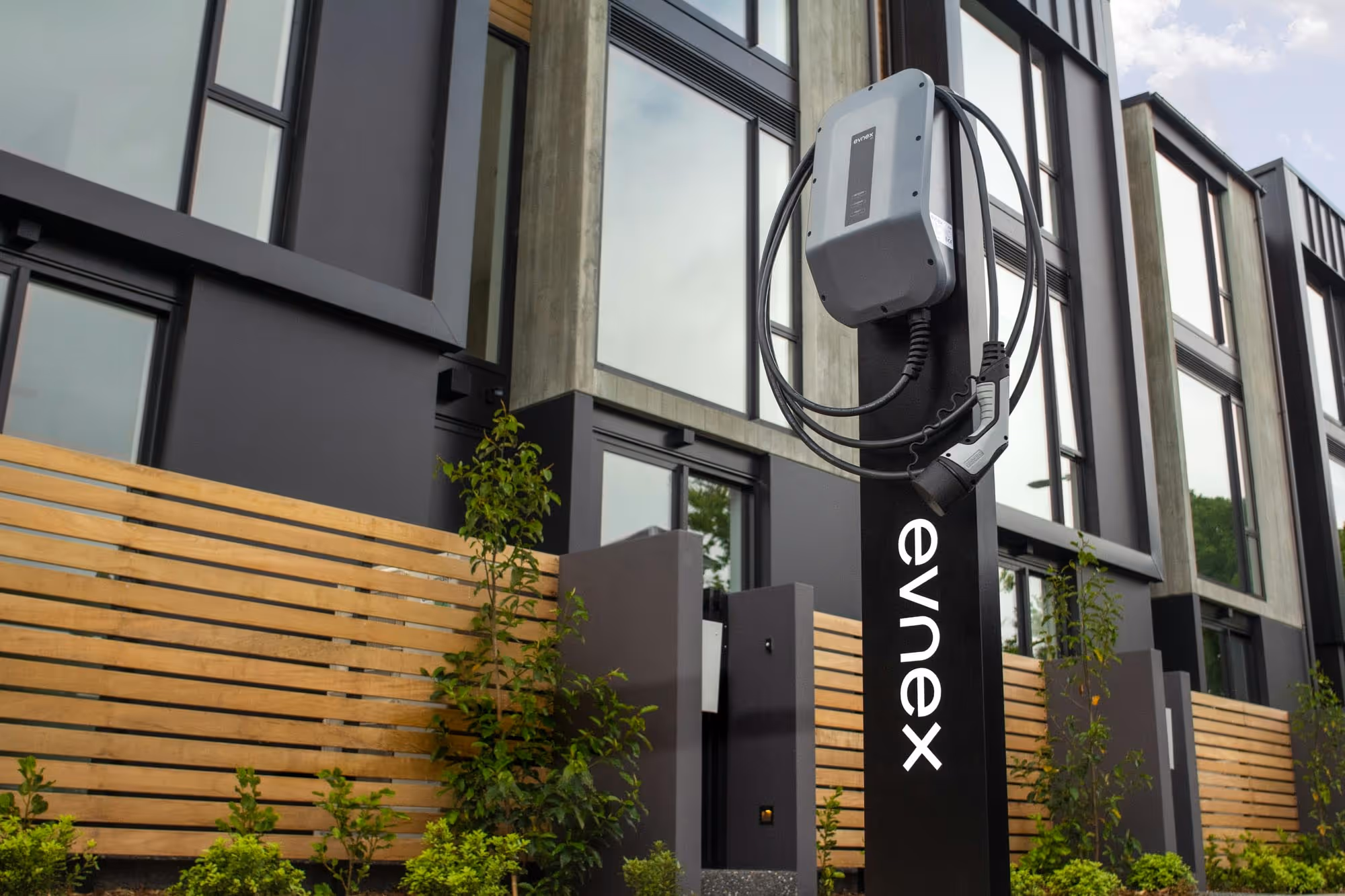 An electrical vehicle charging station with a coiled cable is installed outside modern buildings.