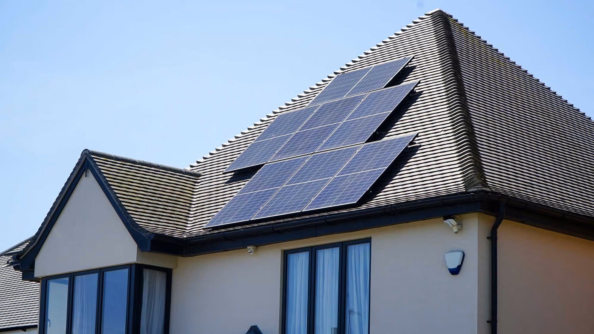 A house with solar panels installed on the roof, under a clear blue sky.