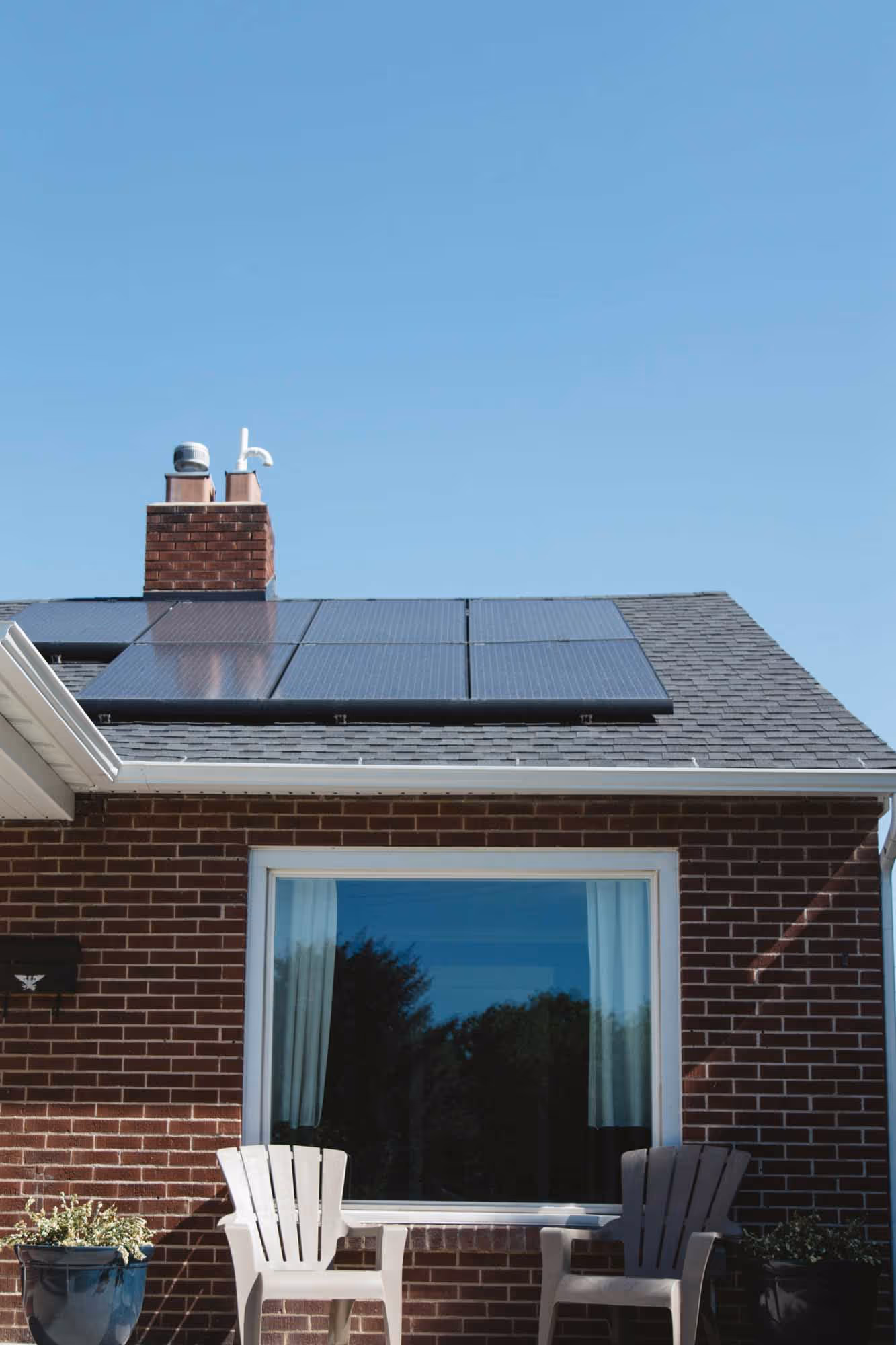 Two chairs and a table on a patio, with solar panels on the roof above.