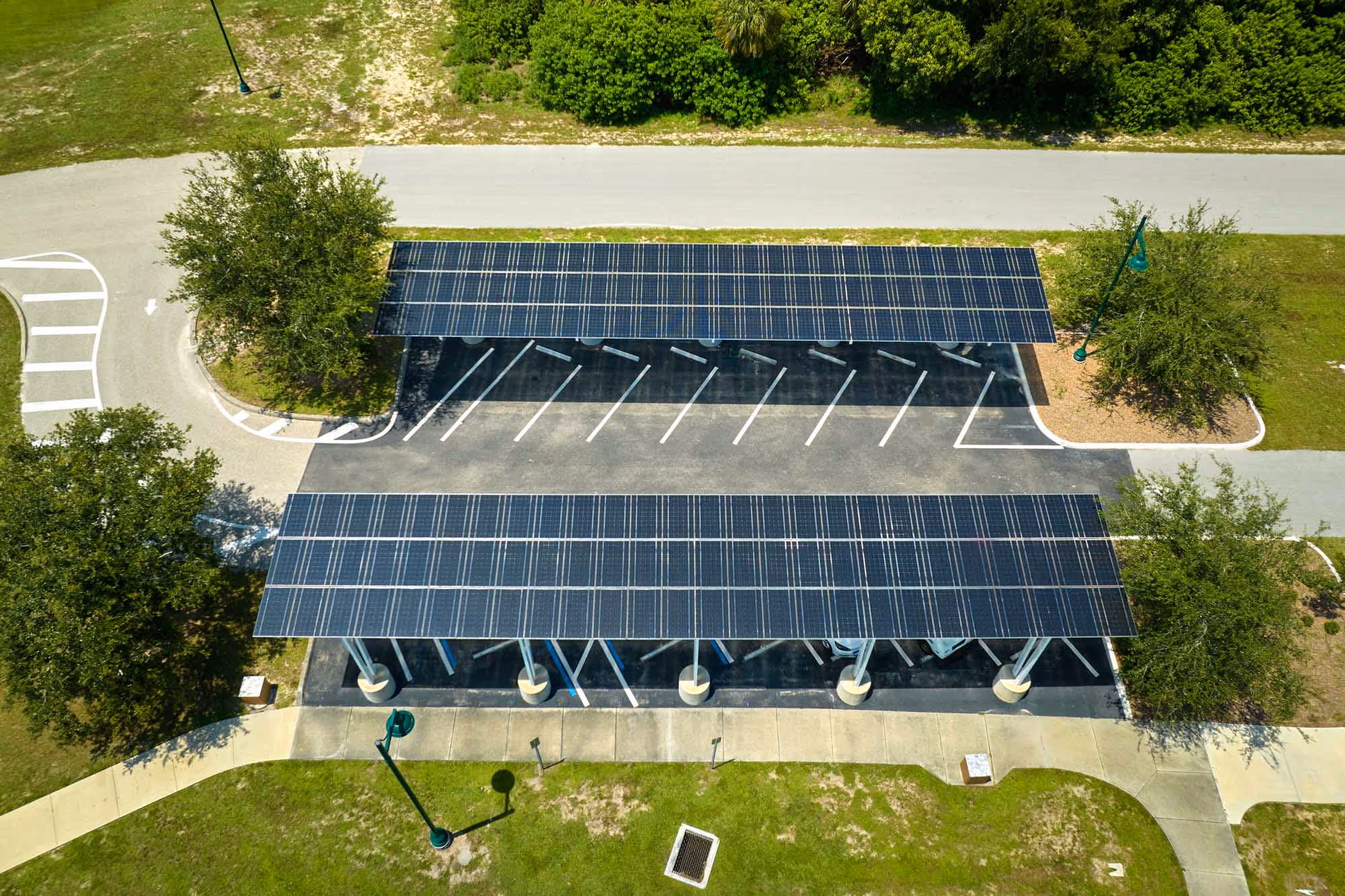Covered parking lot with solar panels on the roof, surrounded by grass and a few trees.