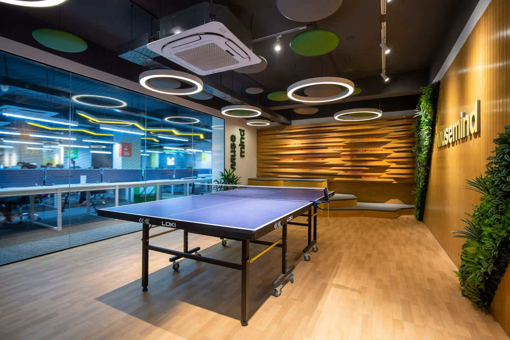 A ping pong table in a modern office space with wooden flooring and stylish circular lighting.