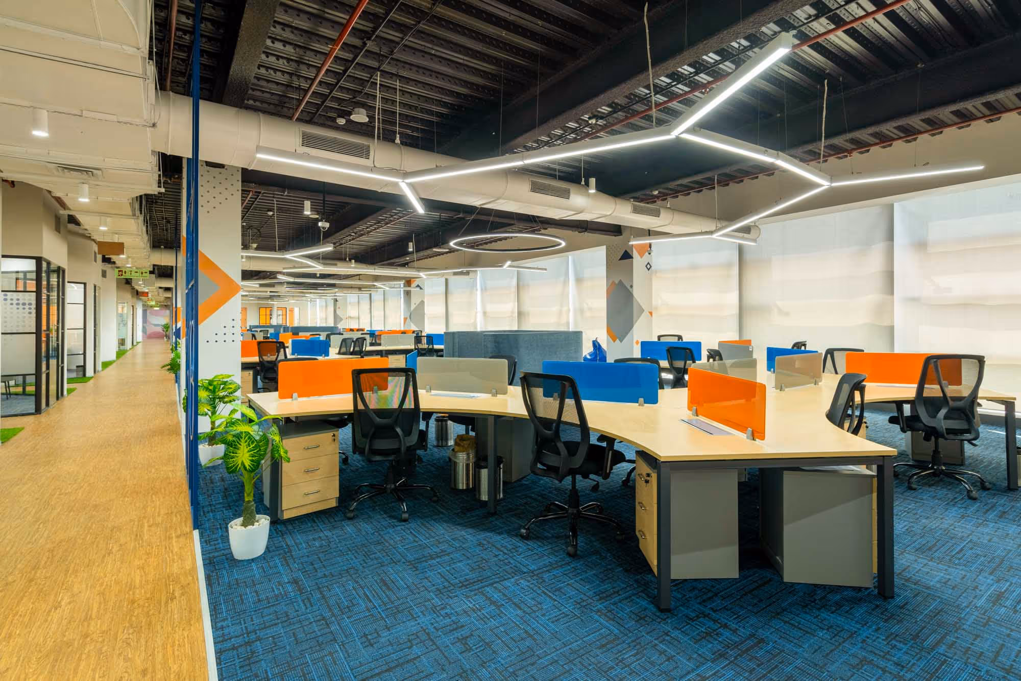 A modern office space with several empty desks and chairs, featuring colorful partitions and bright lighting.