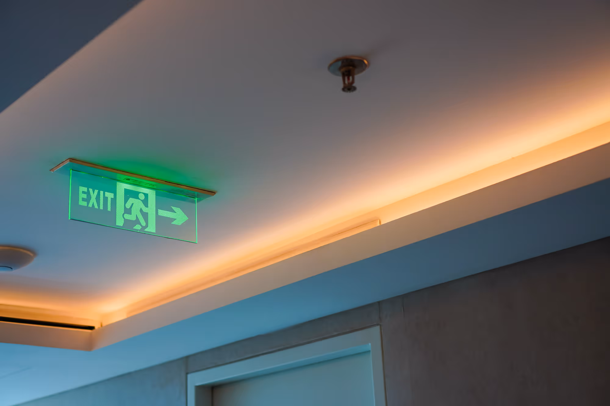 A green exit sign with a running figure and arrow is mounted on a ceiling.