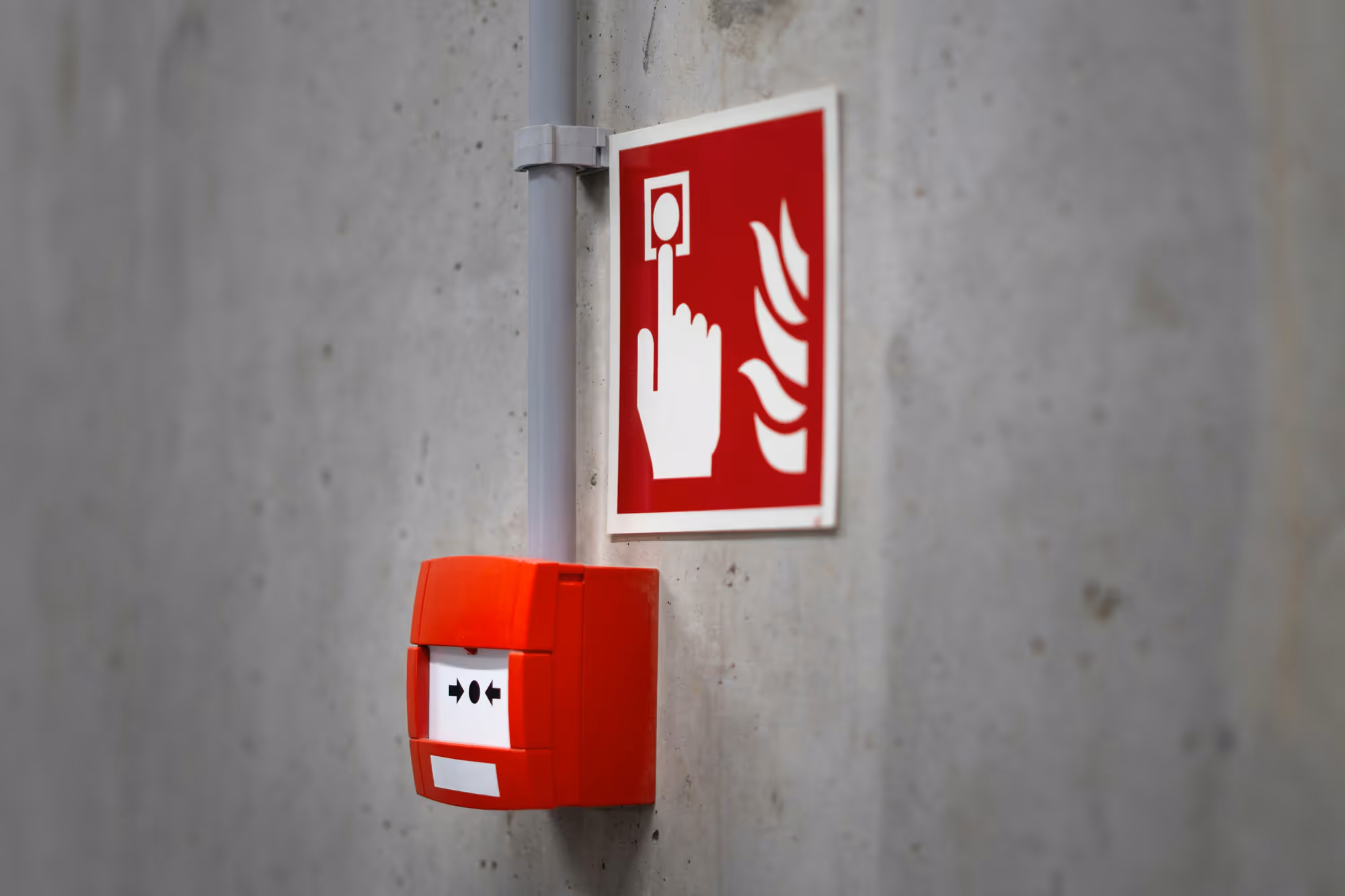 A red fire alarm and an instruction sign are mounted on a concrete wall.