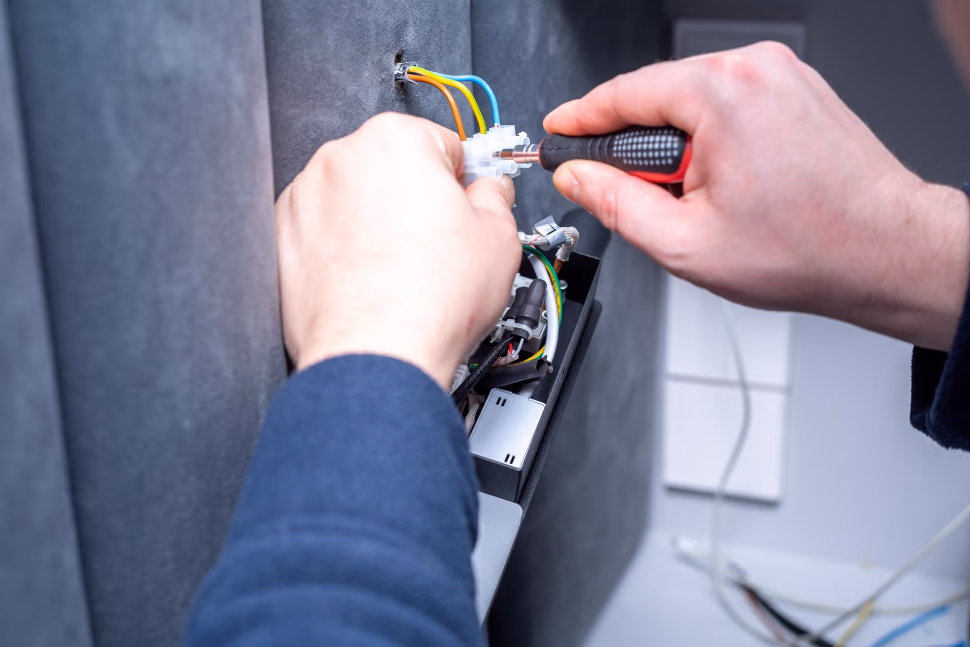 A person uses a screwdriver to connect electrical wires to a device on a wall.