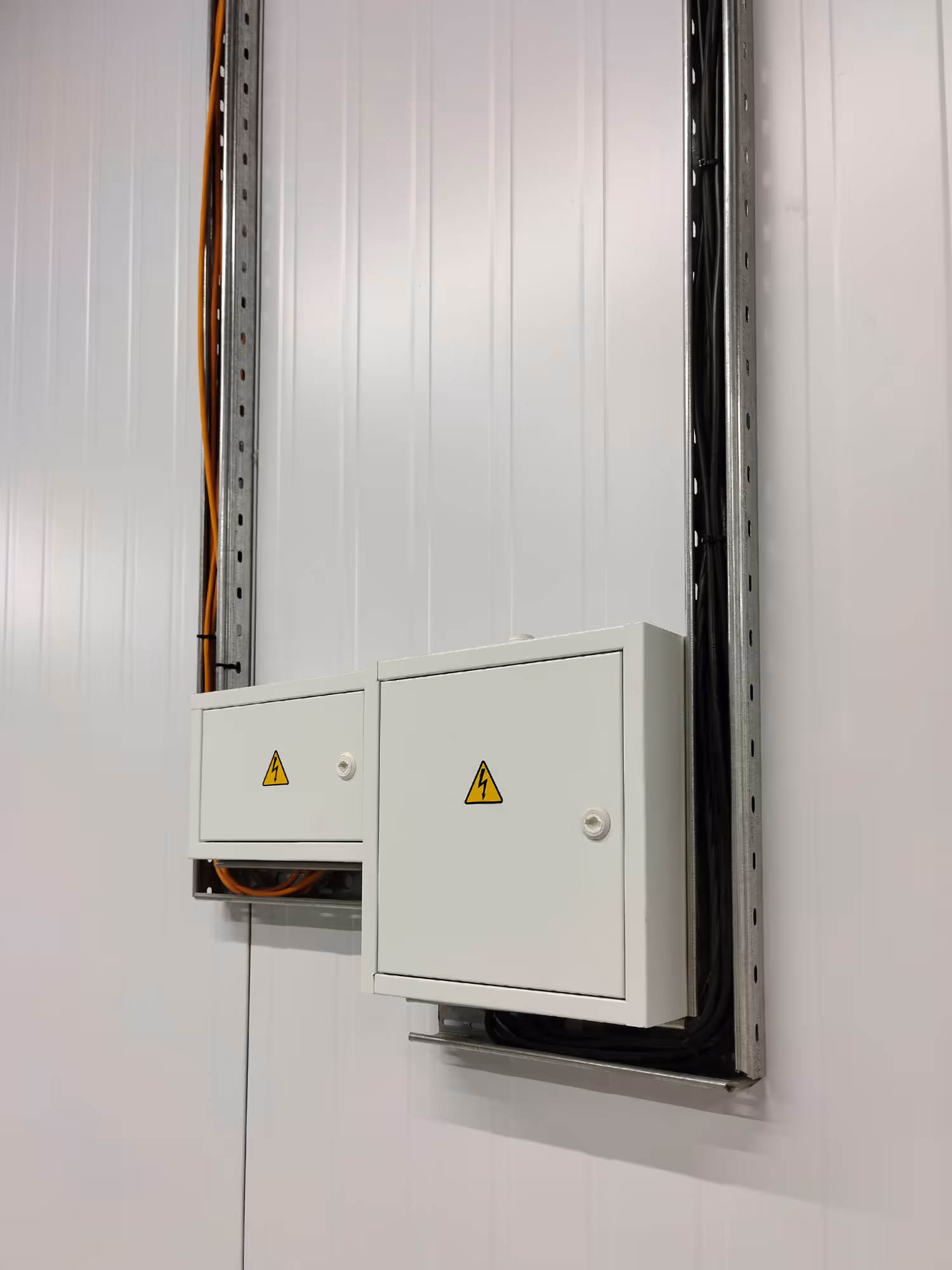 Two white electrical boxes with warning symbols on a wall, cables are visible going into them.