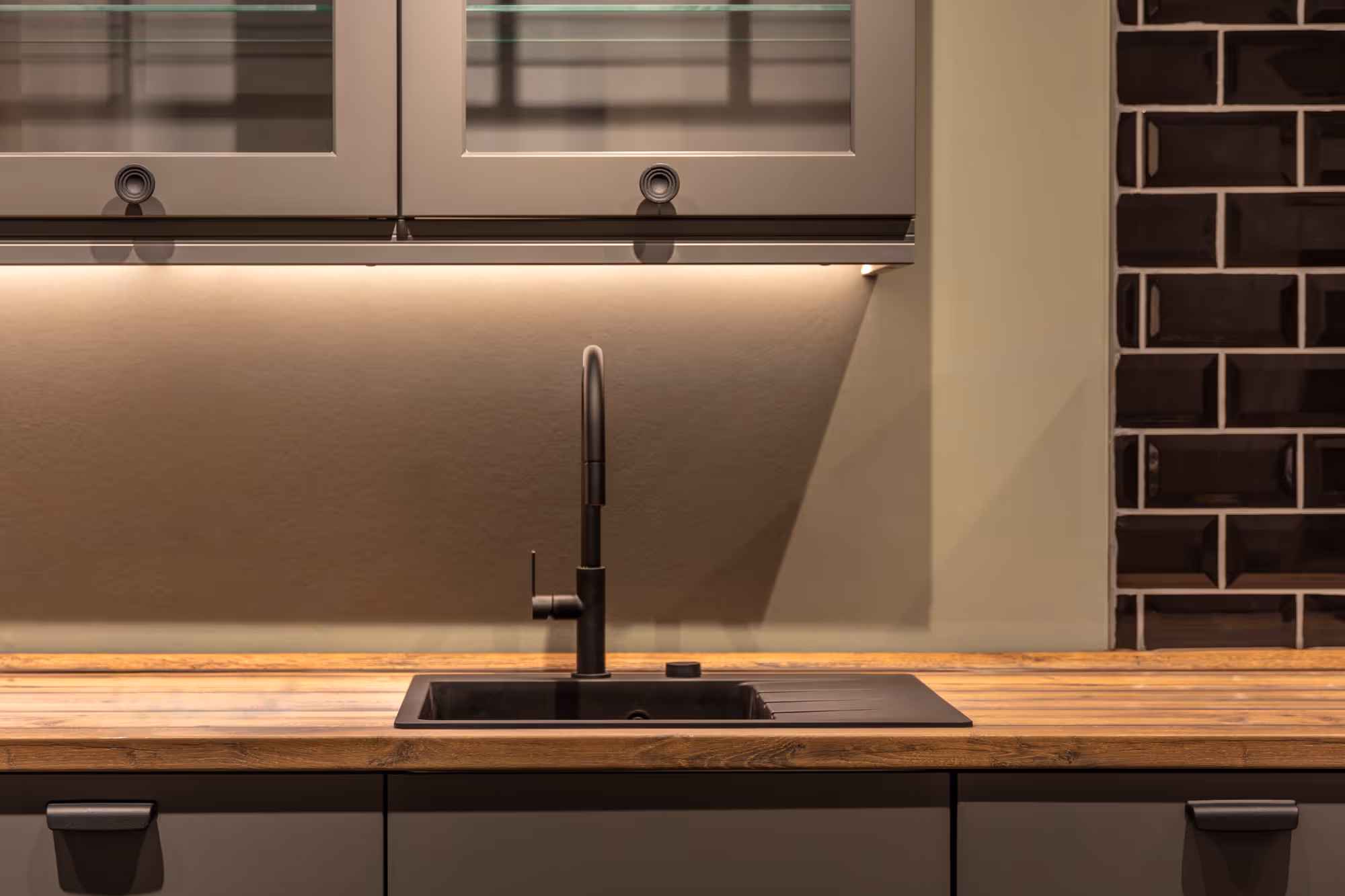 A kitchen sink with a tall faucet is set in a wooden countertop.