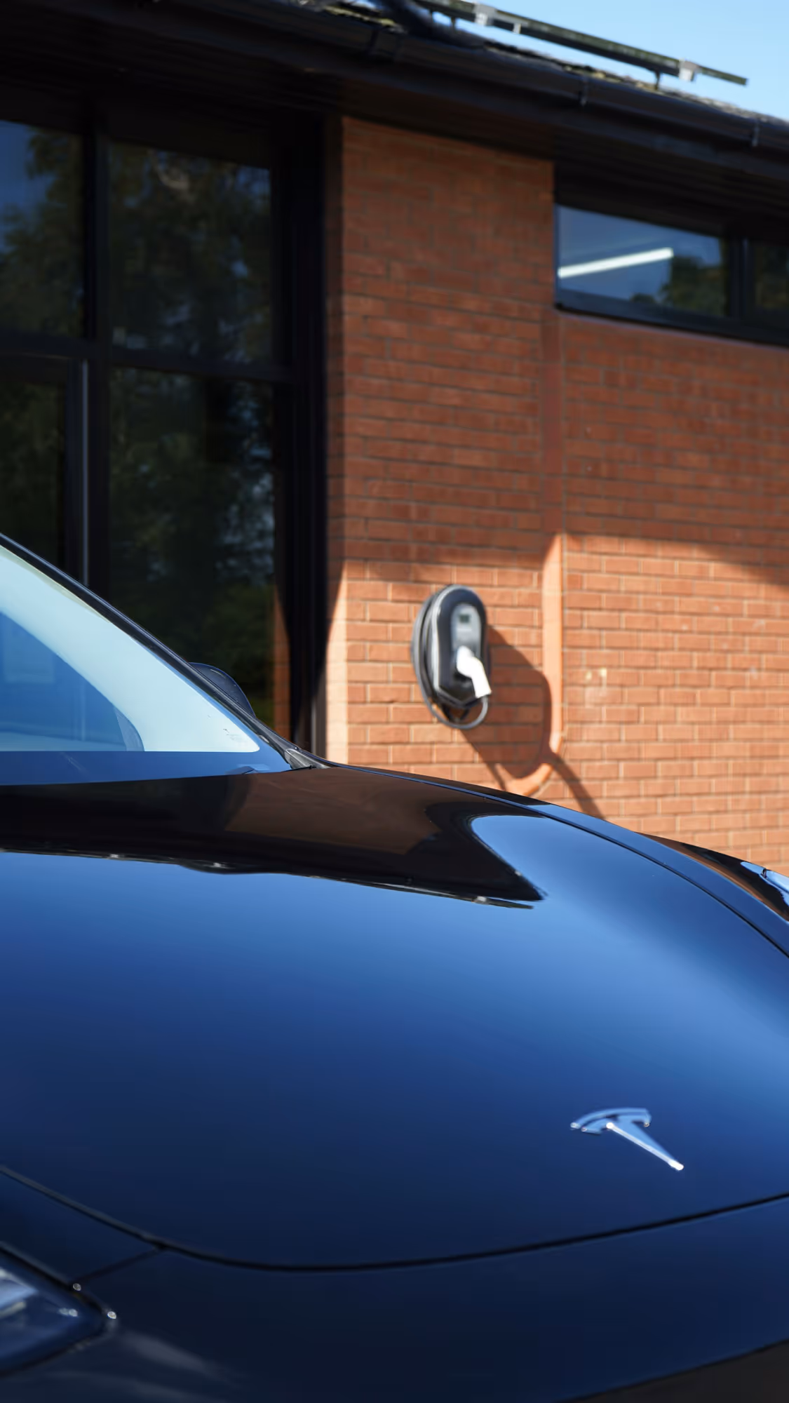 A black car is parked near a brick wall with an electric charging station.