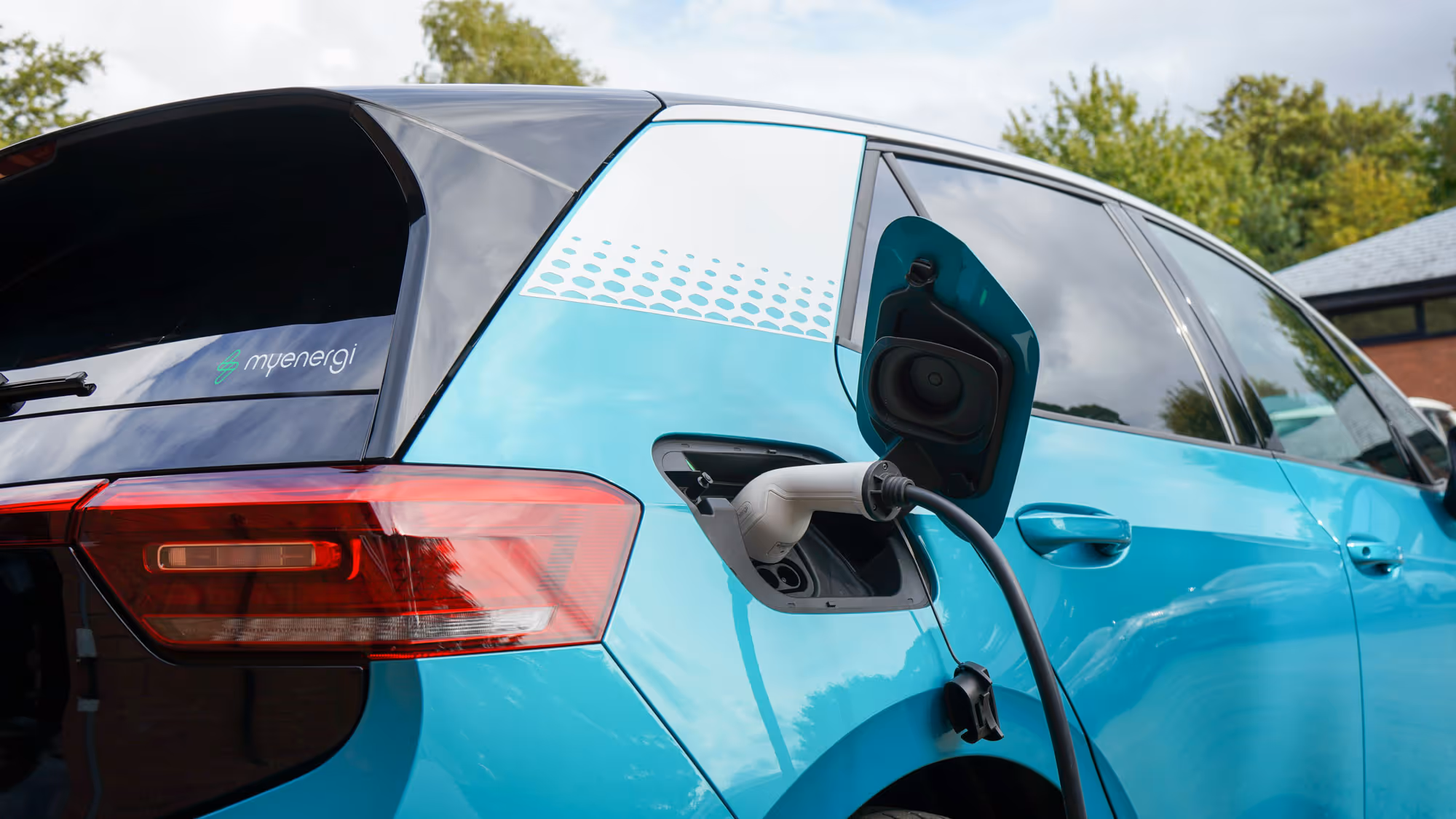 An electric car is being charged, with the charging cable plugged into the car's port.
