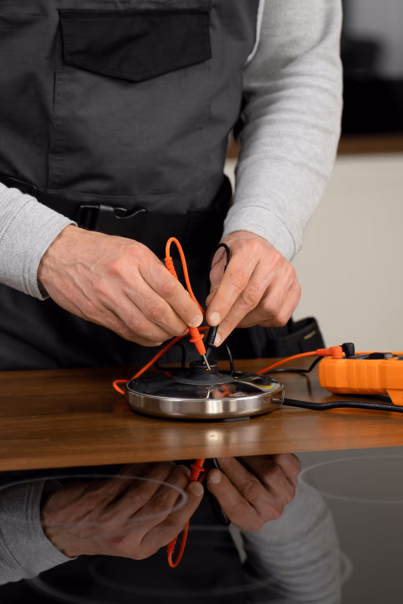 A person uses multimeter probes to test an electrical device on a wooden table.