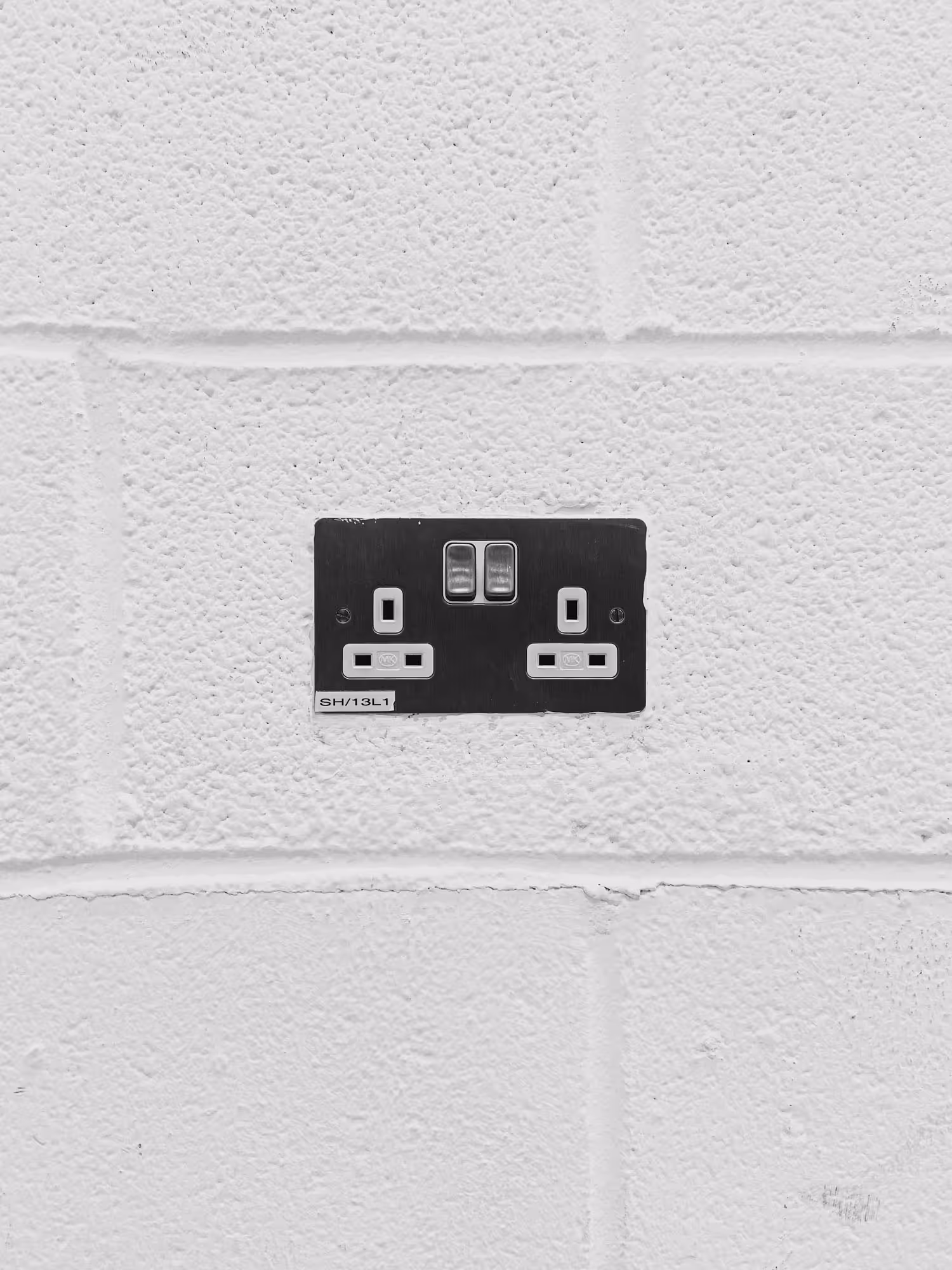 A white wall with a double electrical outlet featuring two plug sockets and a switch.