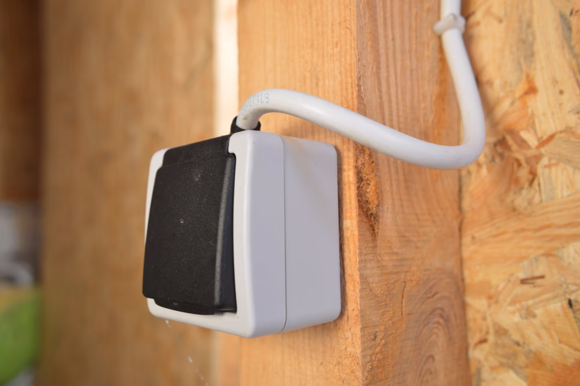 A black and white outdoor electrical socket with a closed cover on a wooden wall.