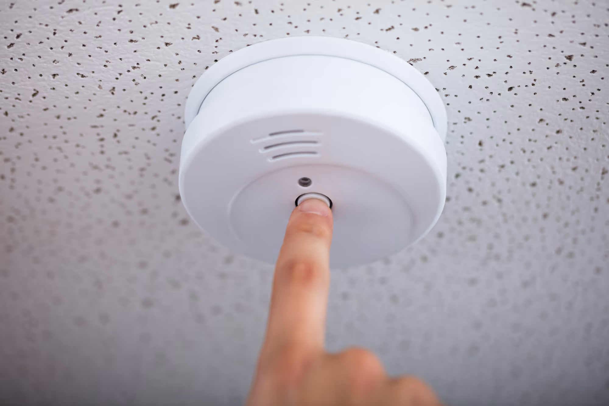 Person pressing a button on a ceiling-mounted smoke detector.
