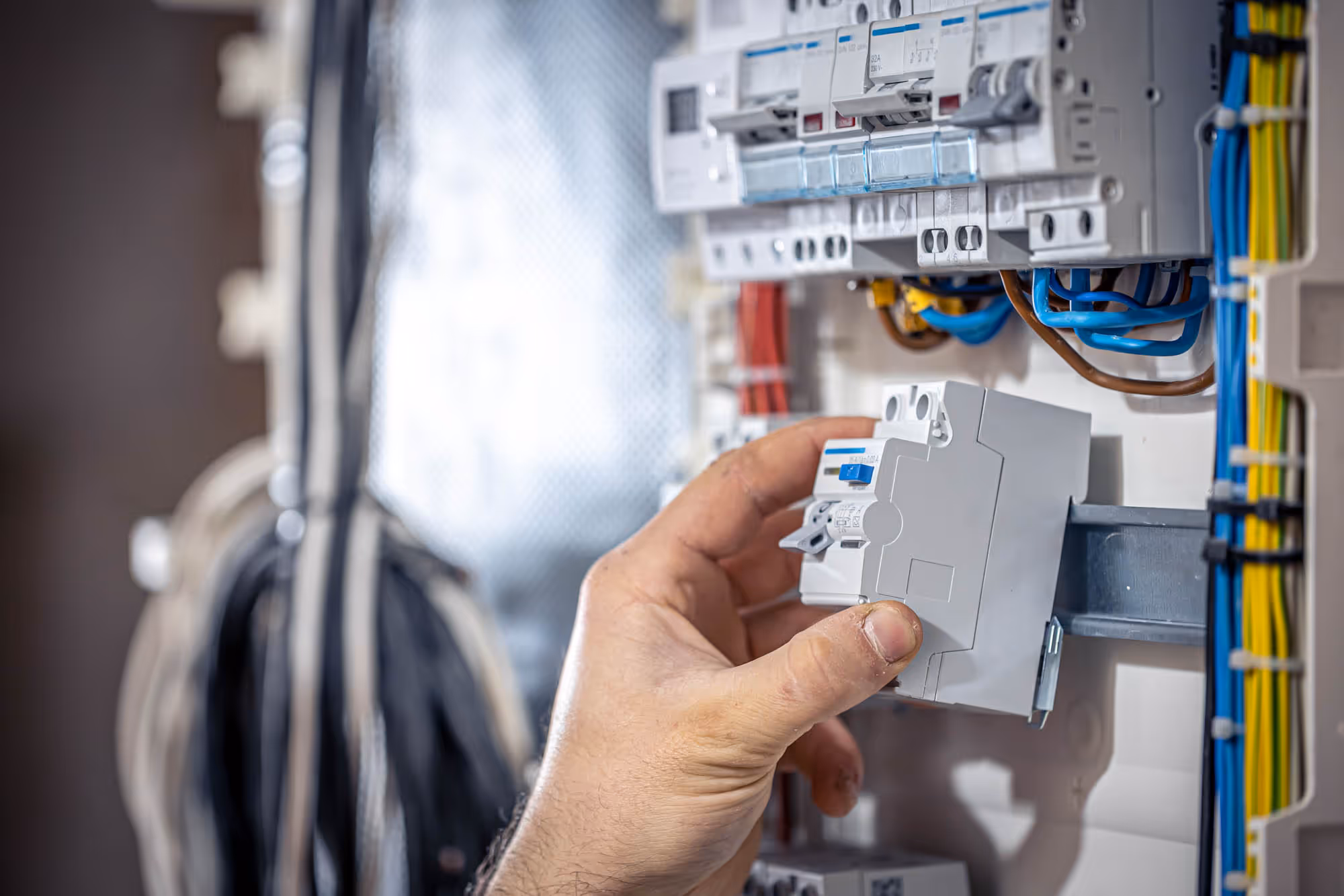 A person's hand installs a breaker into an electrical panel.