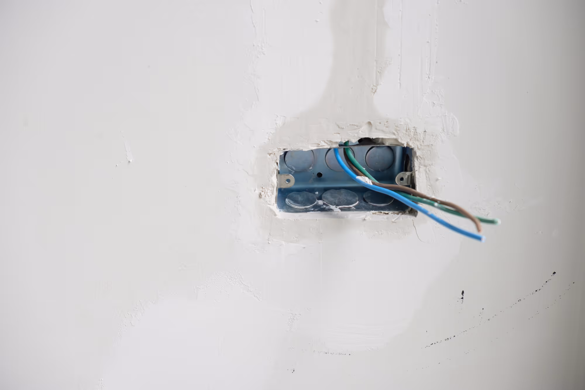 A wall with visible electrical wires protruding from an open electric box.