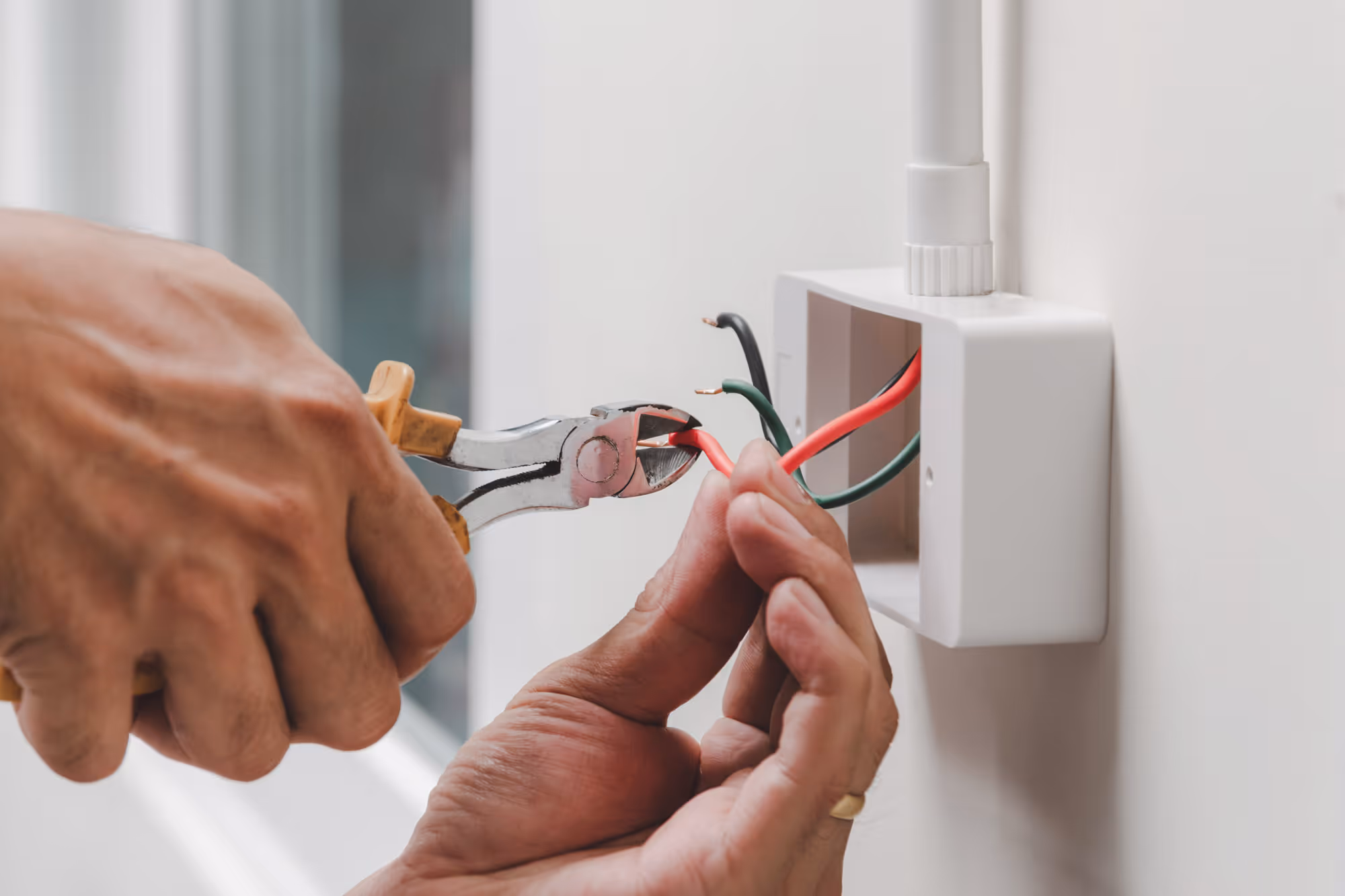 Person uses pliers to cut wires connected to an electrical outlet box.