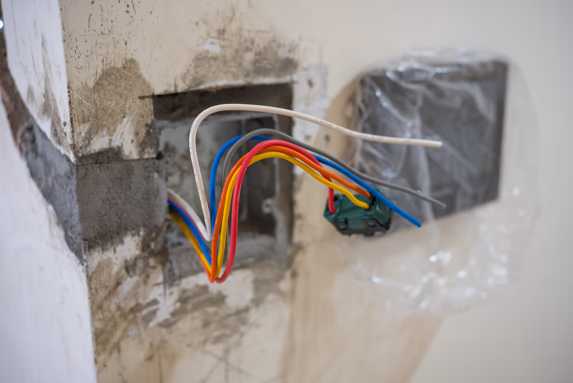 Exposed electrical wires protrude from a wall socket, with different colored insulation visible.