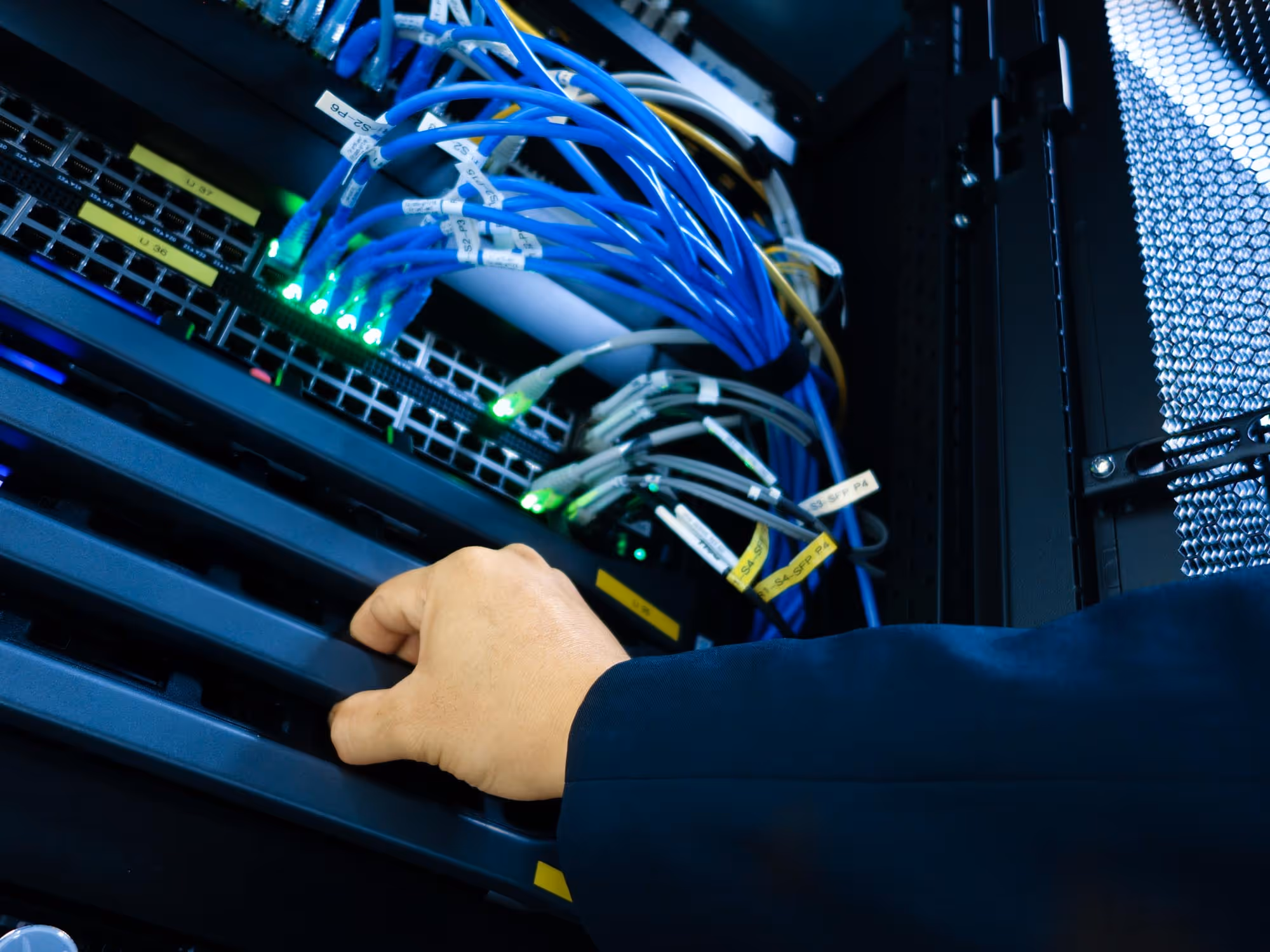 A person adjusts cables and equipment inside a server rack containing network switches and wires.