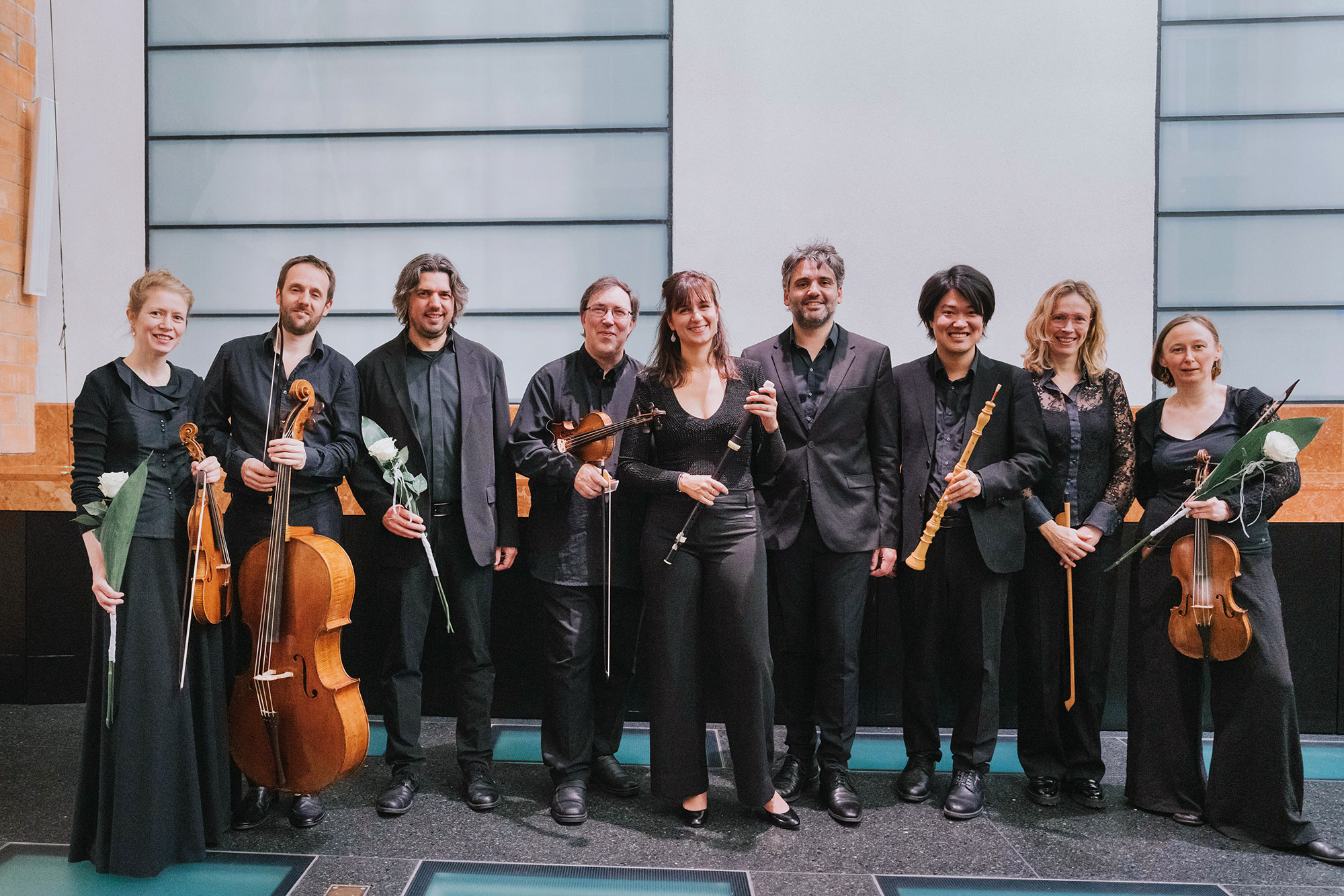 Orchestra and choir performing on stage with conductor in spotlight, surrounded by string instruments and harpsichord.