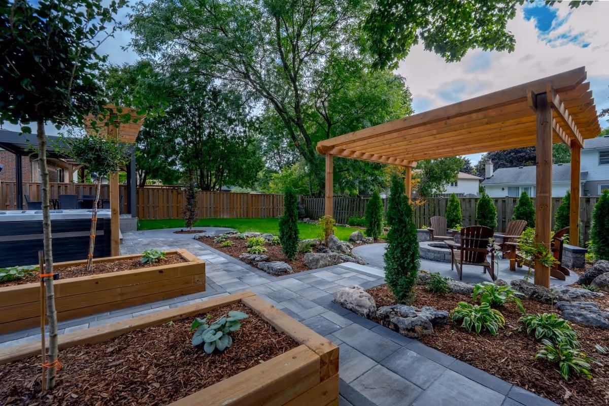 Well-maintained backyard with paved walkways, raised wooden garden beds, small evergreen trees, and a wooden pergola with seating underneath.
