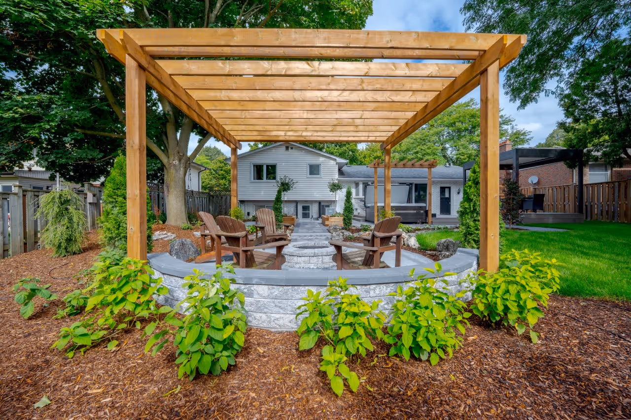 Backyard with wooden pergola over a stone fire pit area surrounded by Adirondack chairs and landscaping.