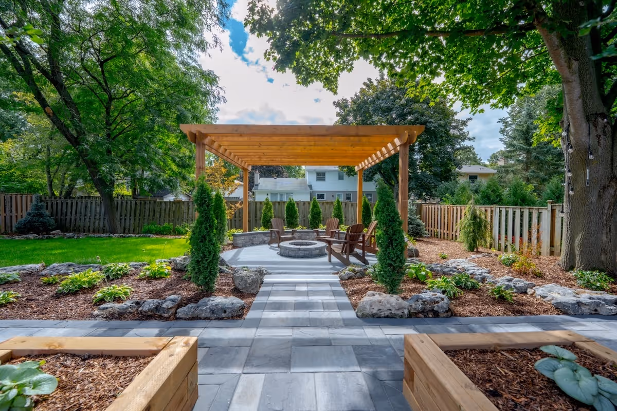Backyard seating area with wooden pergola, stone fire pit, Adirondack chairs, surrounded by greenery and a wooden fence.