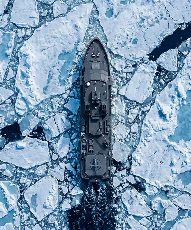 Aerial view of a black icebreaker ship cutting through broken Arctic sea ice.