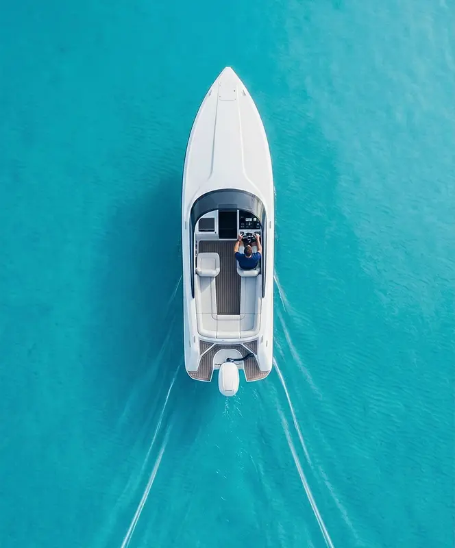A white motorboat with a person steering, viewed from above on clear turquoise water.