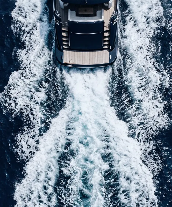 A boat moving fast through dark blue water, creating white foam trails behind it.