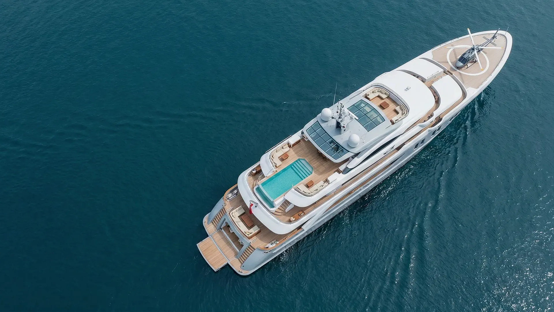 Luxury yacht with a swimming pool and helicopter on deck sailing on calm blue water.