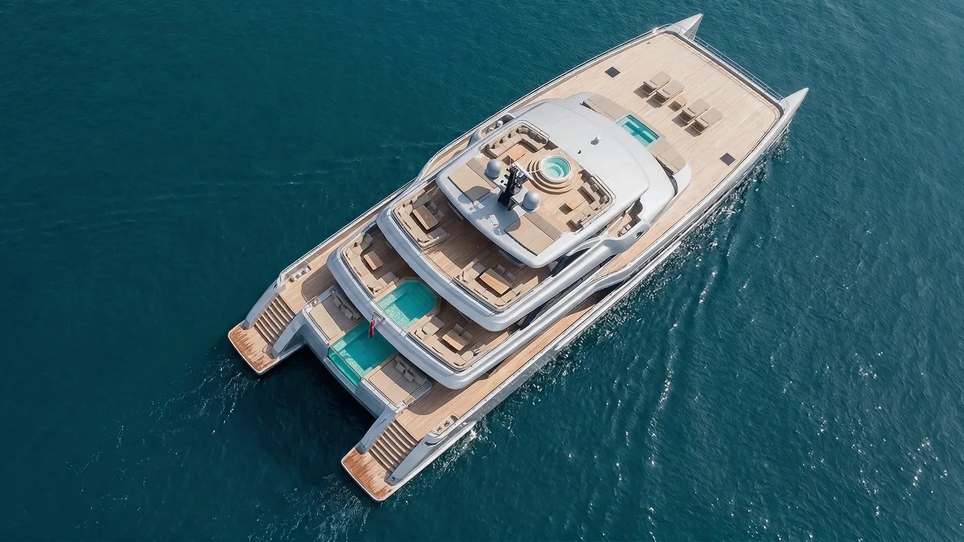 Aerial view of a luxury yacht with multiple decks, pools, sun loungers, and a hot tub on the ocean.