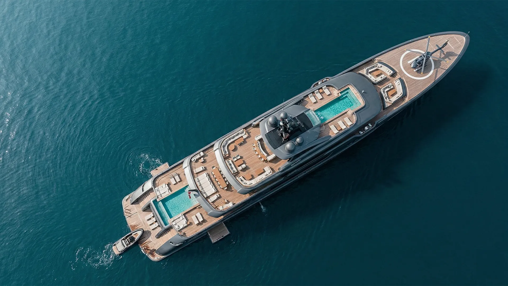 Aerial view of a luxury yacht with three pools, several sun loungers, and a helicopter on deck.