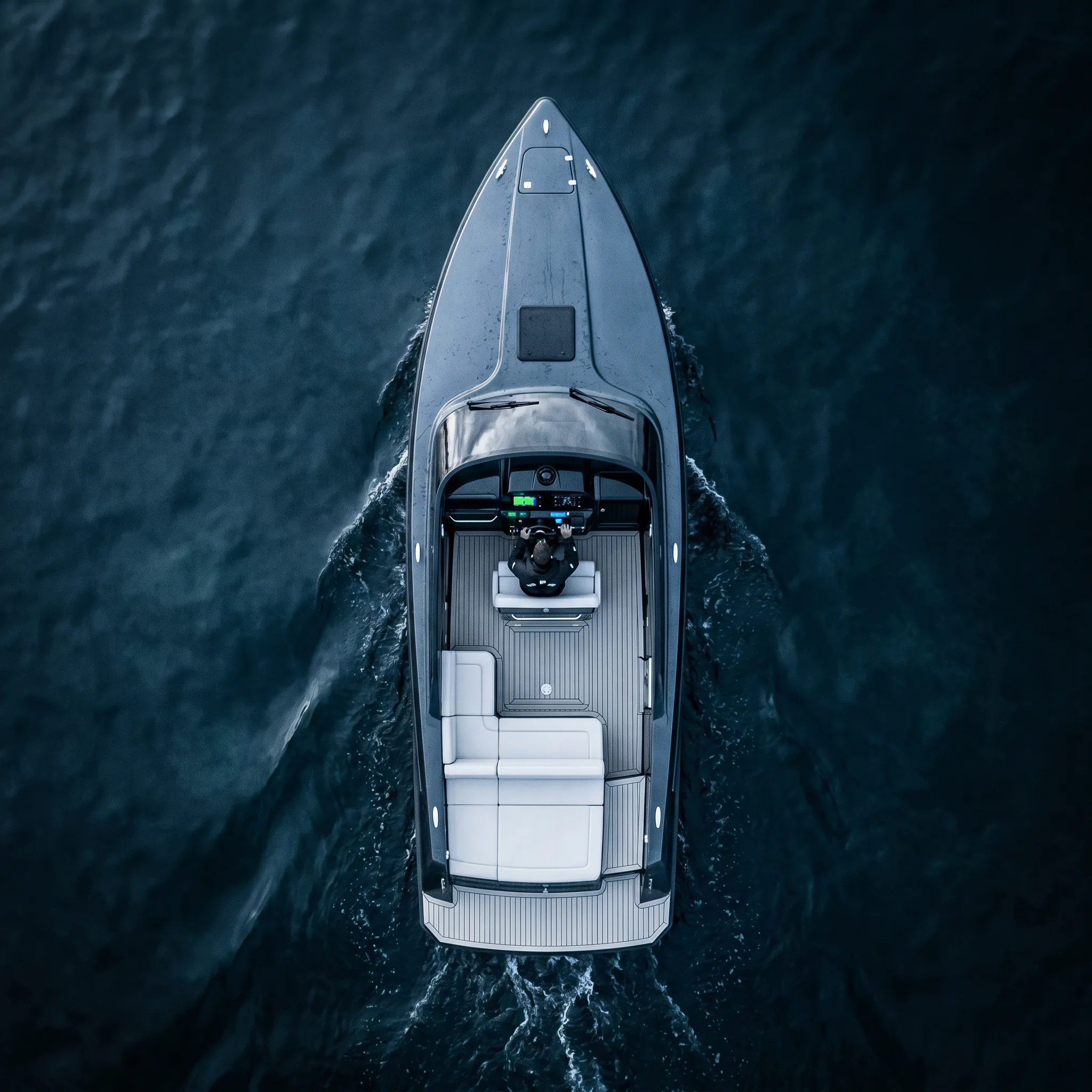 Top-down view of a person steering a sleek motorboat on dark water leaving a wake behind.