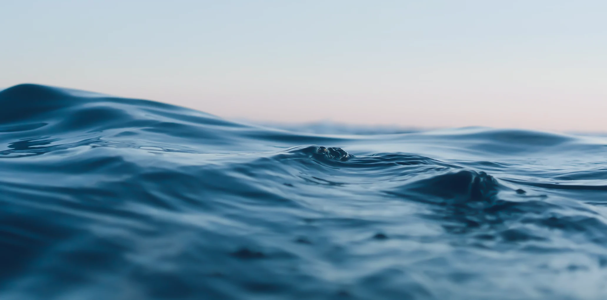 Close-up of gently rolling blue ocean waves under a clear sky at dawn or dusk.