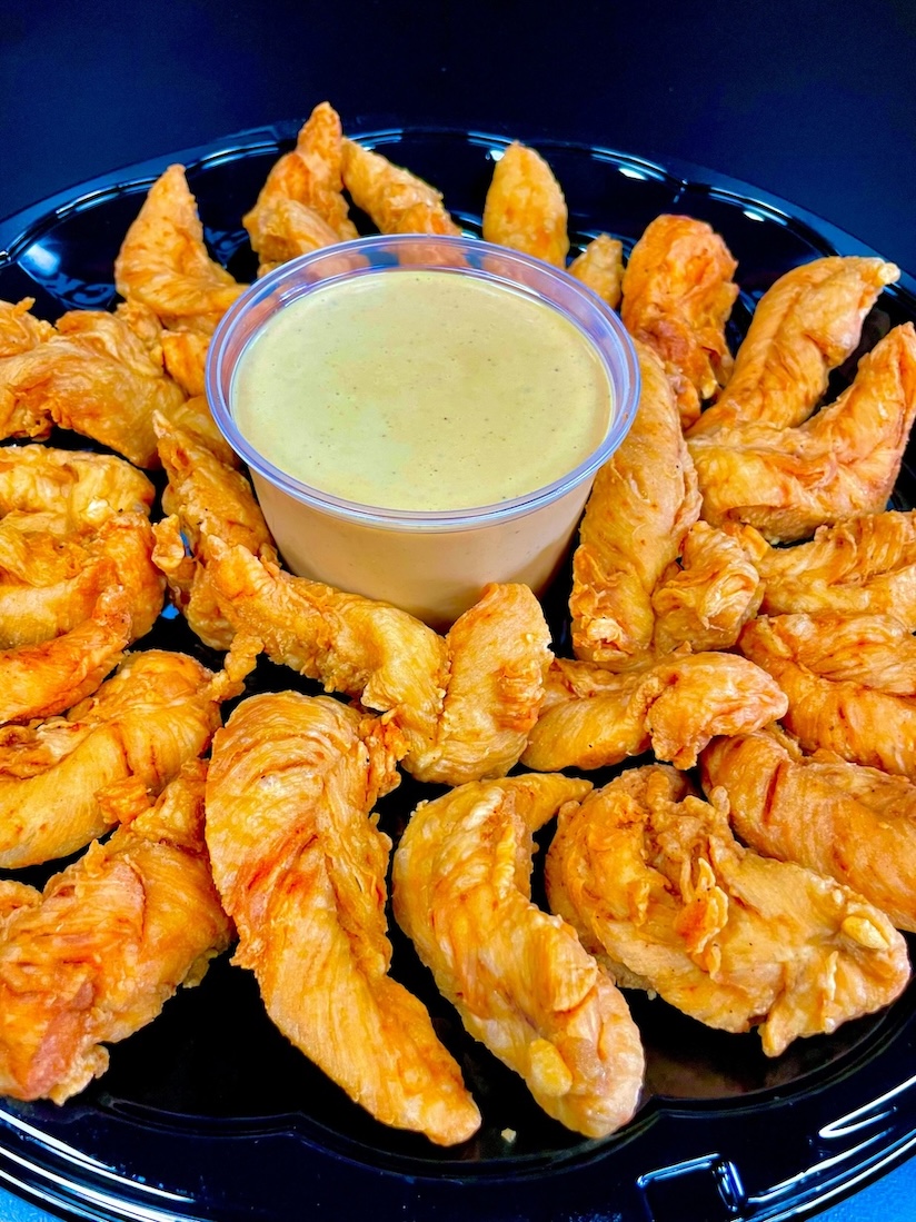 Tray of crispy fried chicken tenders arranged around a cup of creamy dipping sauce.