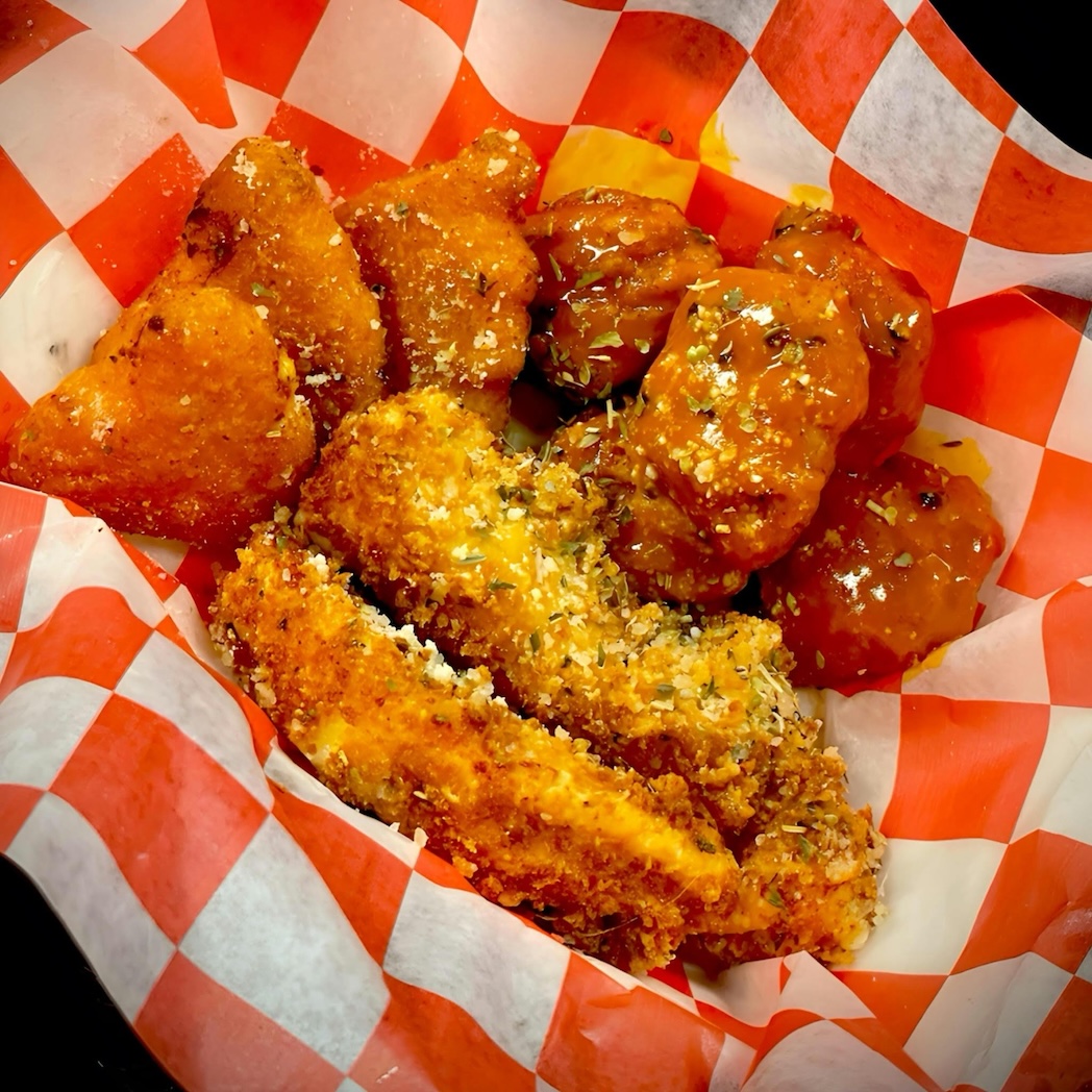 Basket of assorted chicken wings with crispy breaded and sauced pieces on a red and white checkered paper.