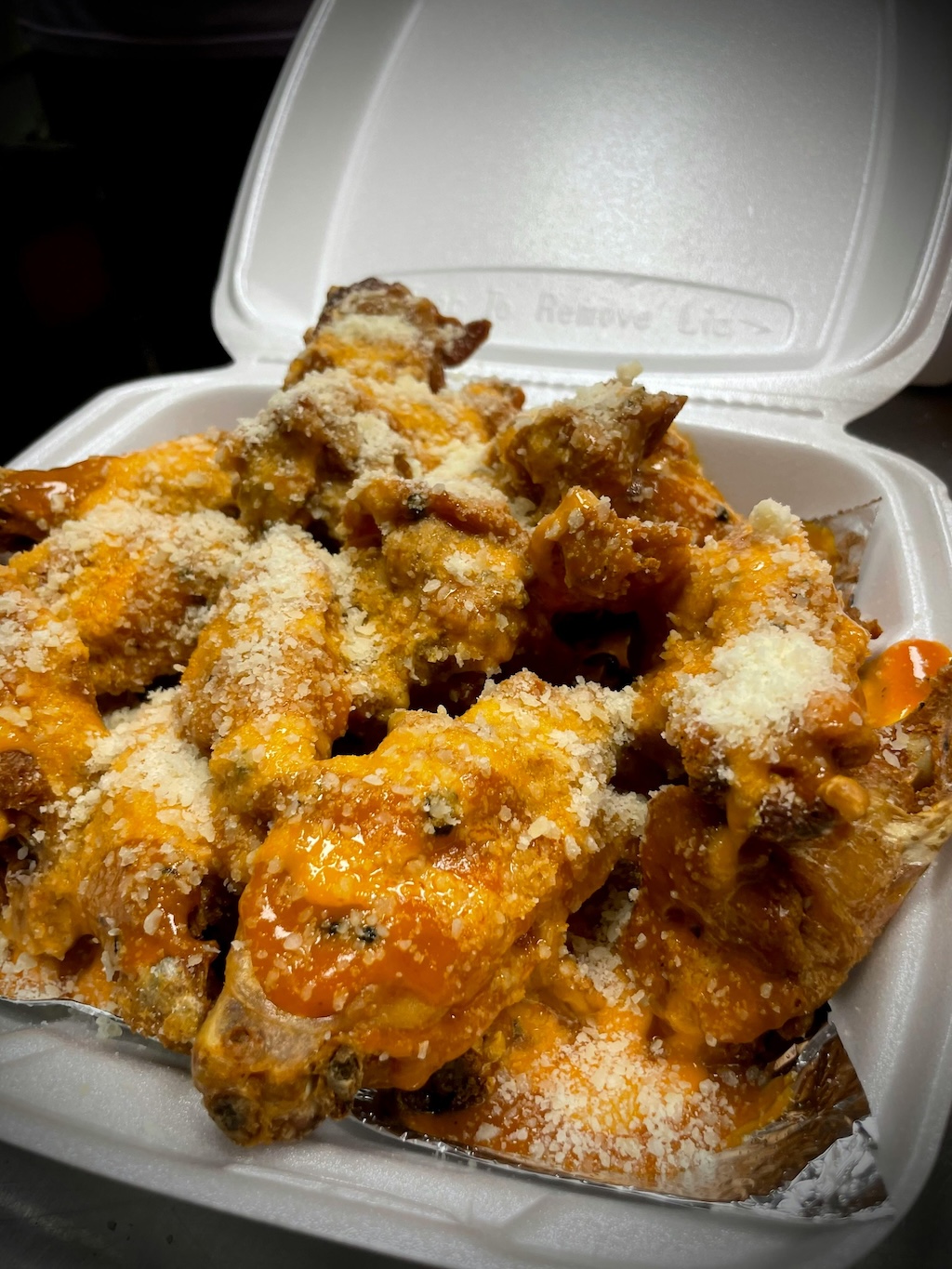 Takeout container filled with buffalo chicken wings topped with grated cheese.
